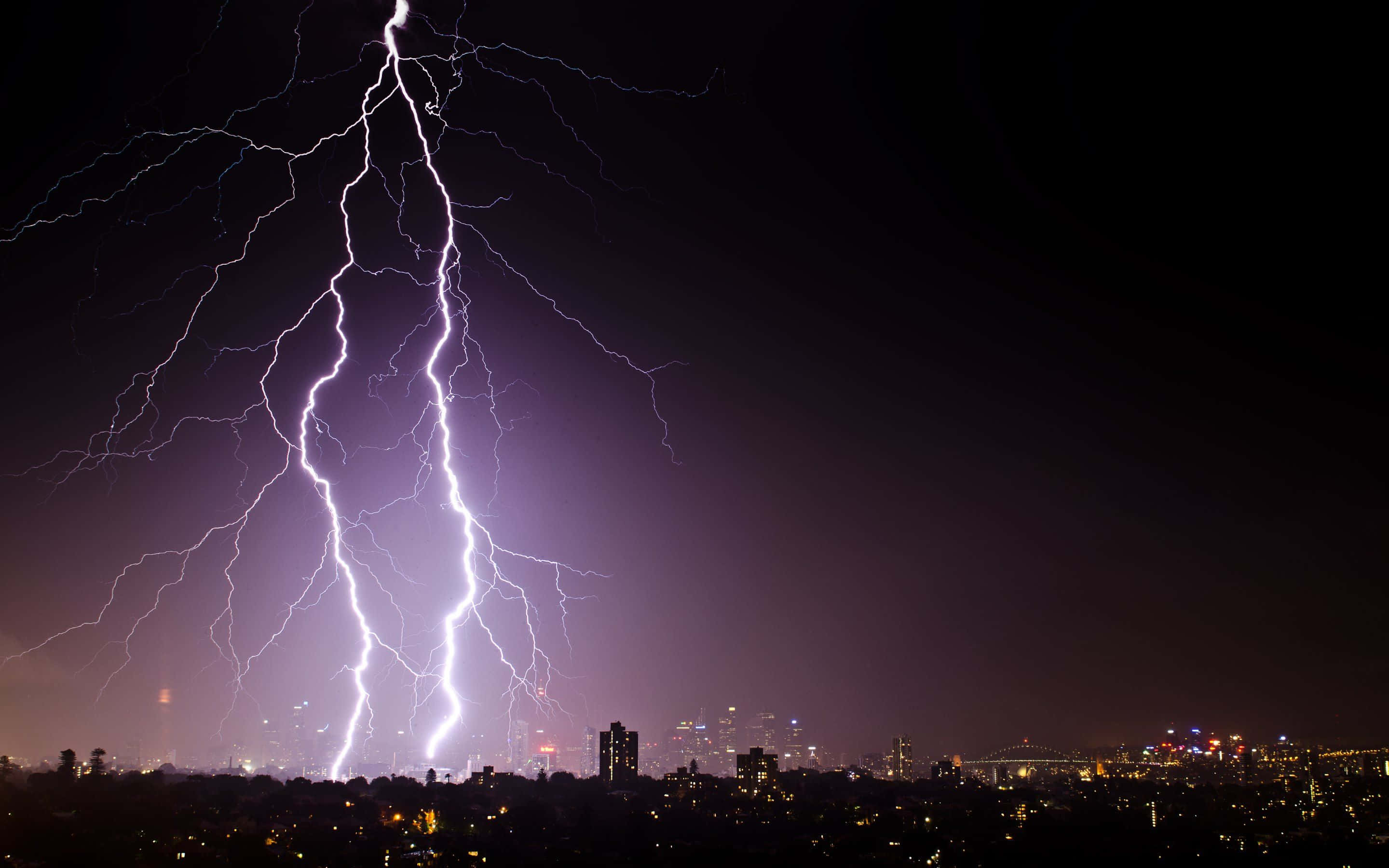迷人雷暴閃電 壁紙 — 一道巨大的閃電照亮了暴風雨夜晚的天空，下方是燈火輝煌的廣闊城市景觀。