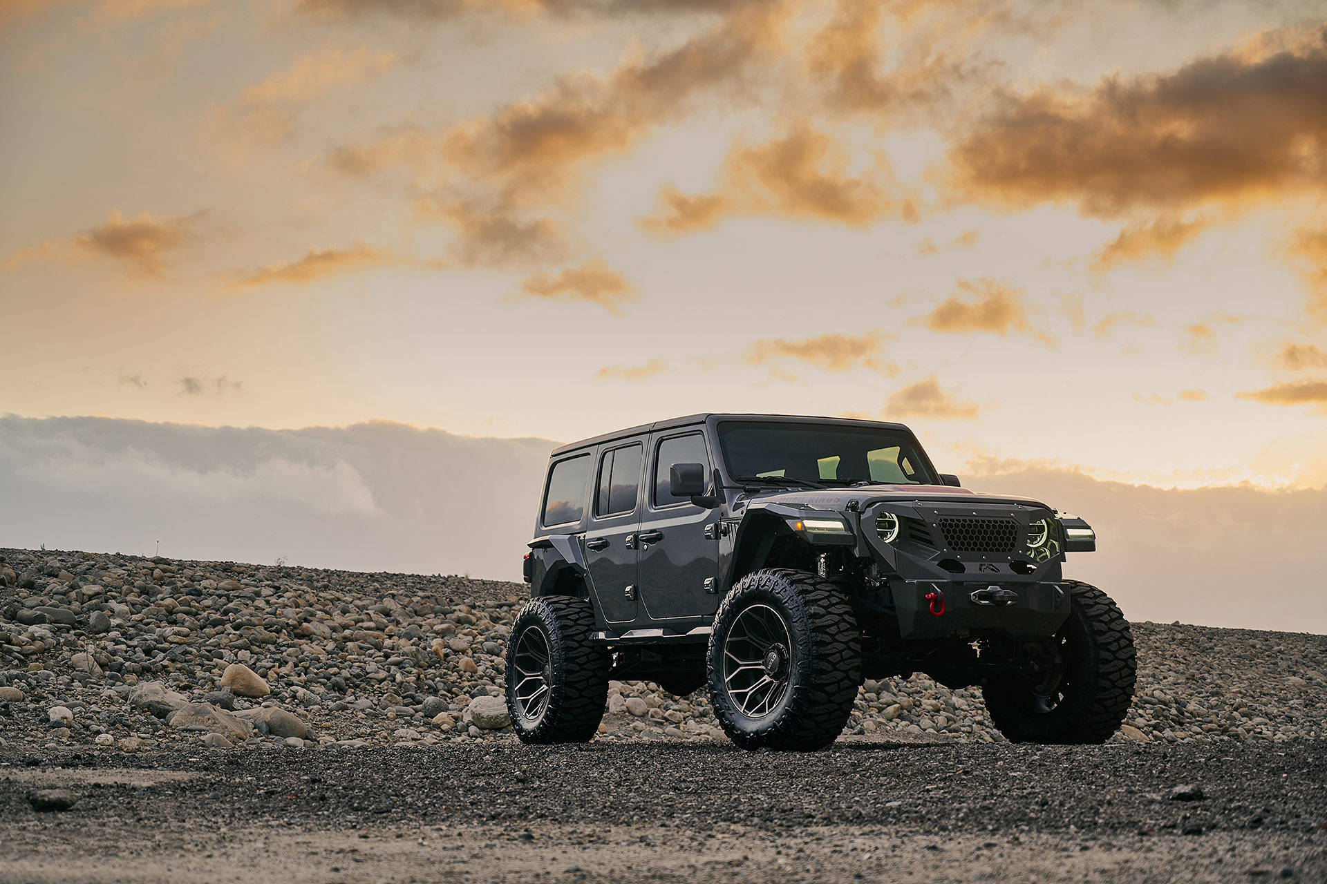 日落時分，一輛灰色Jeep Wrangler停在岩石山坡上。