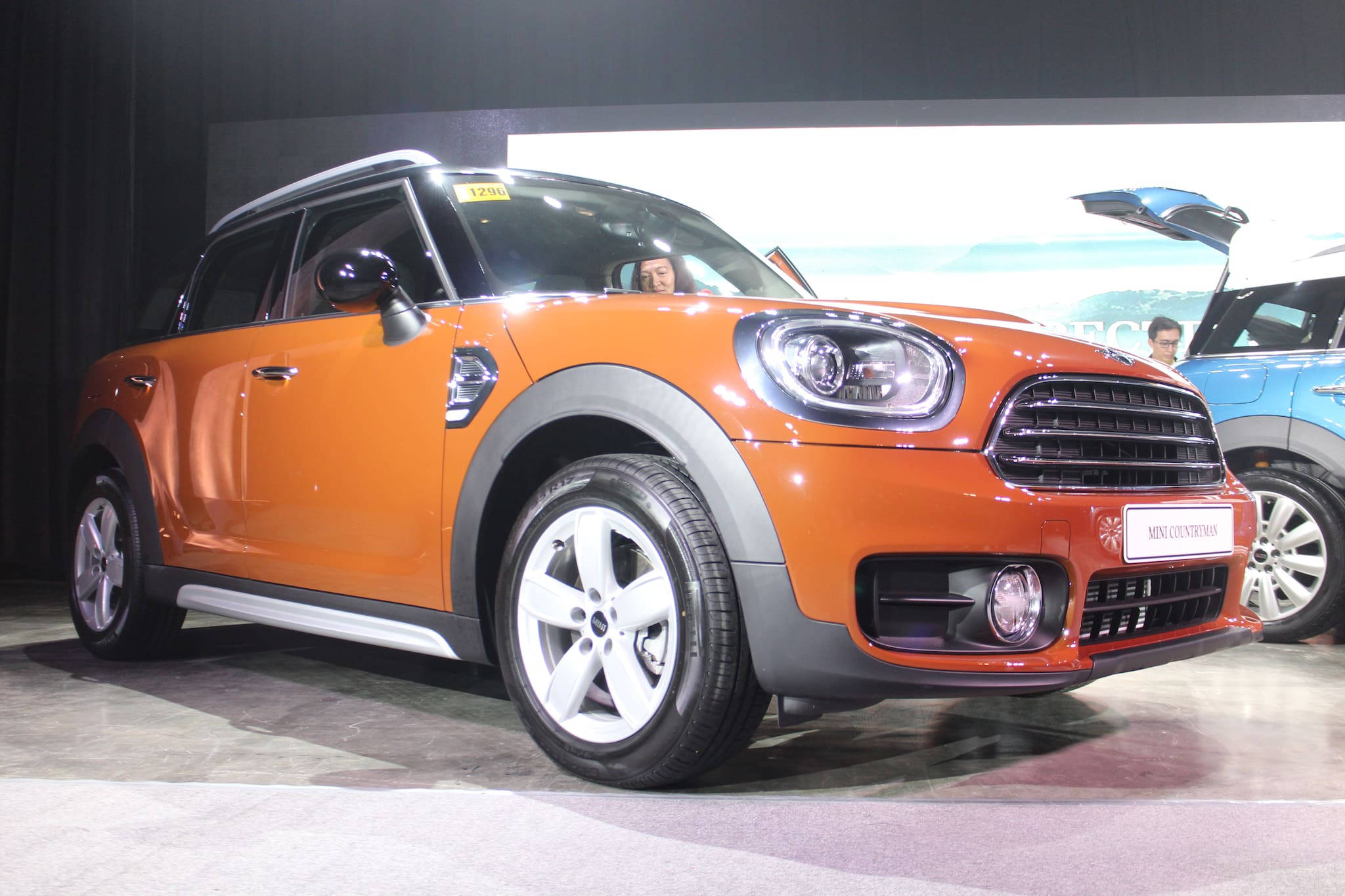 迷你橙色美學汽車 壁紙 — 一輛充滿活力的橙色MINI Countryman SUV在車展的明亮燈光下閃閃發光，車內可見一人。