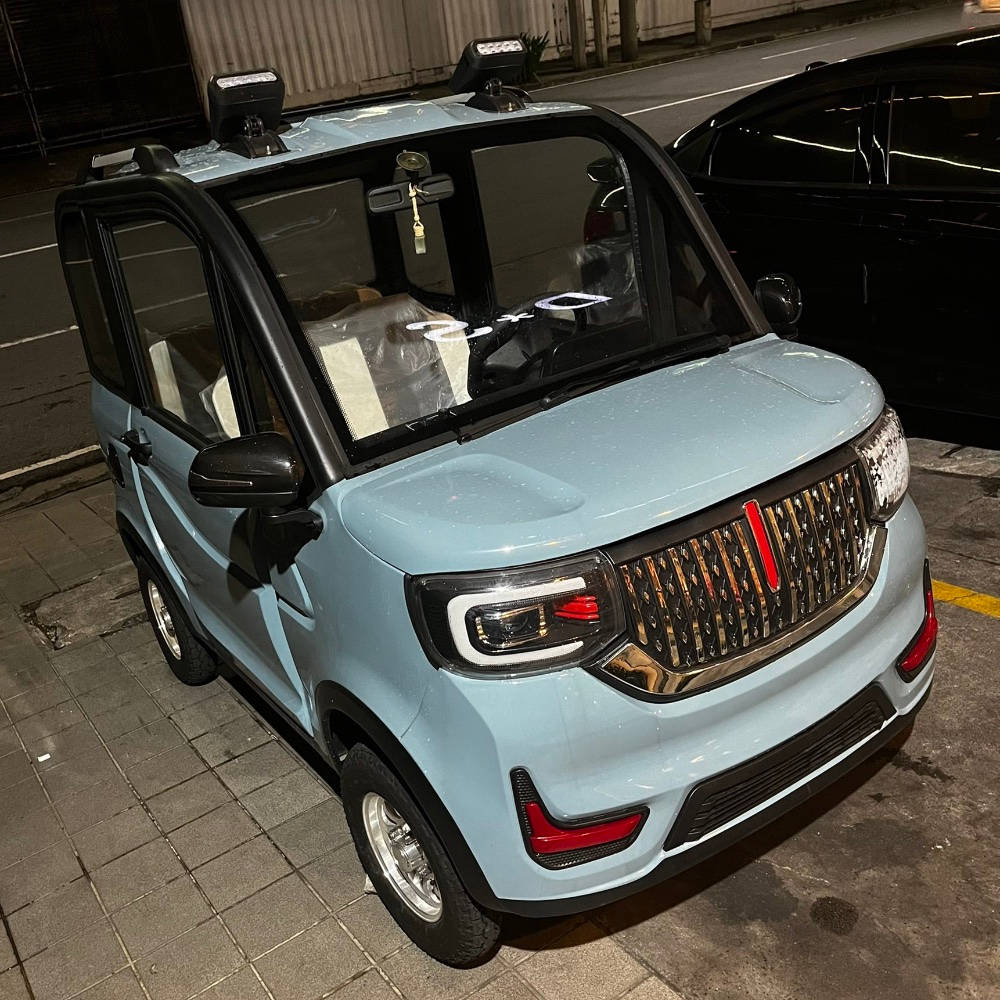 迷你淺藍色車款 壁紙 — 一輛淺藍色緊湊型電動車停在夜間鋪砌的街道上，帶有發光的車頭燈和紅色飾邊。