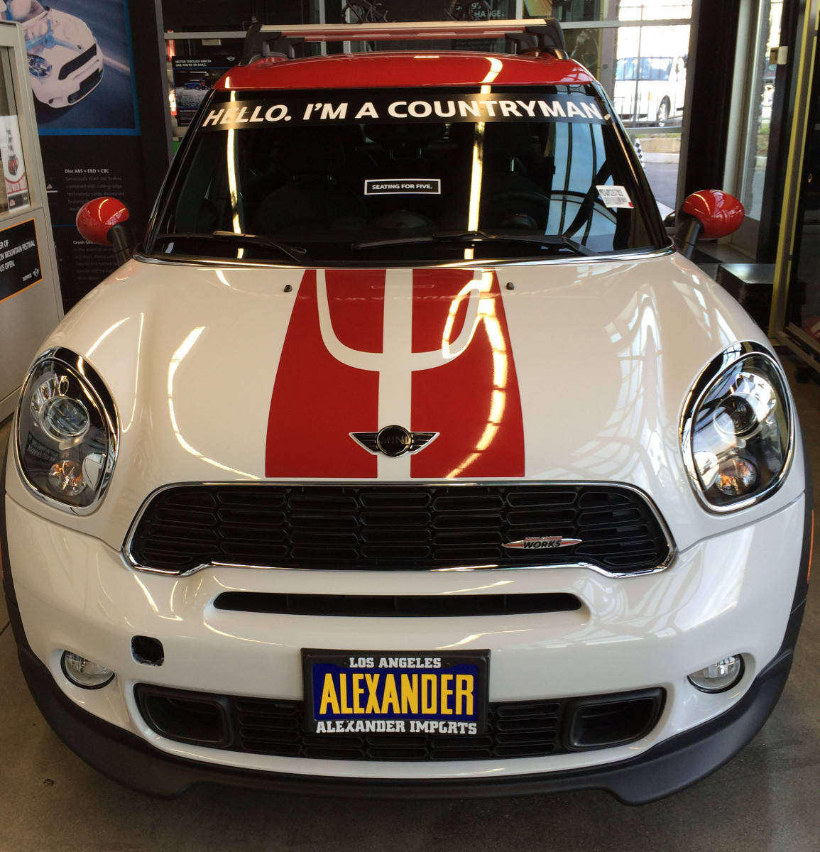 迷你白紅色汽車 壁紙 — 一輛白色MINI Countryman，帶有紅色賽車條紋，擋風玻璃上寫著「HELLO I'M A COUNTRYMAN」，停放在展廳內。