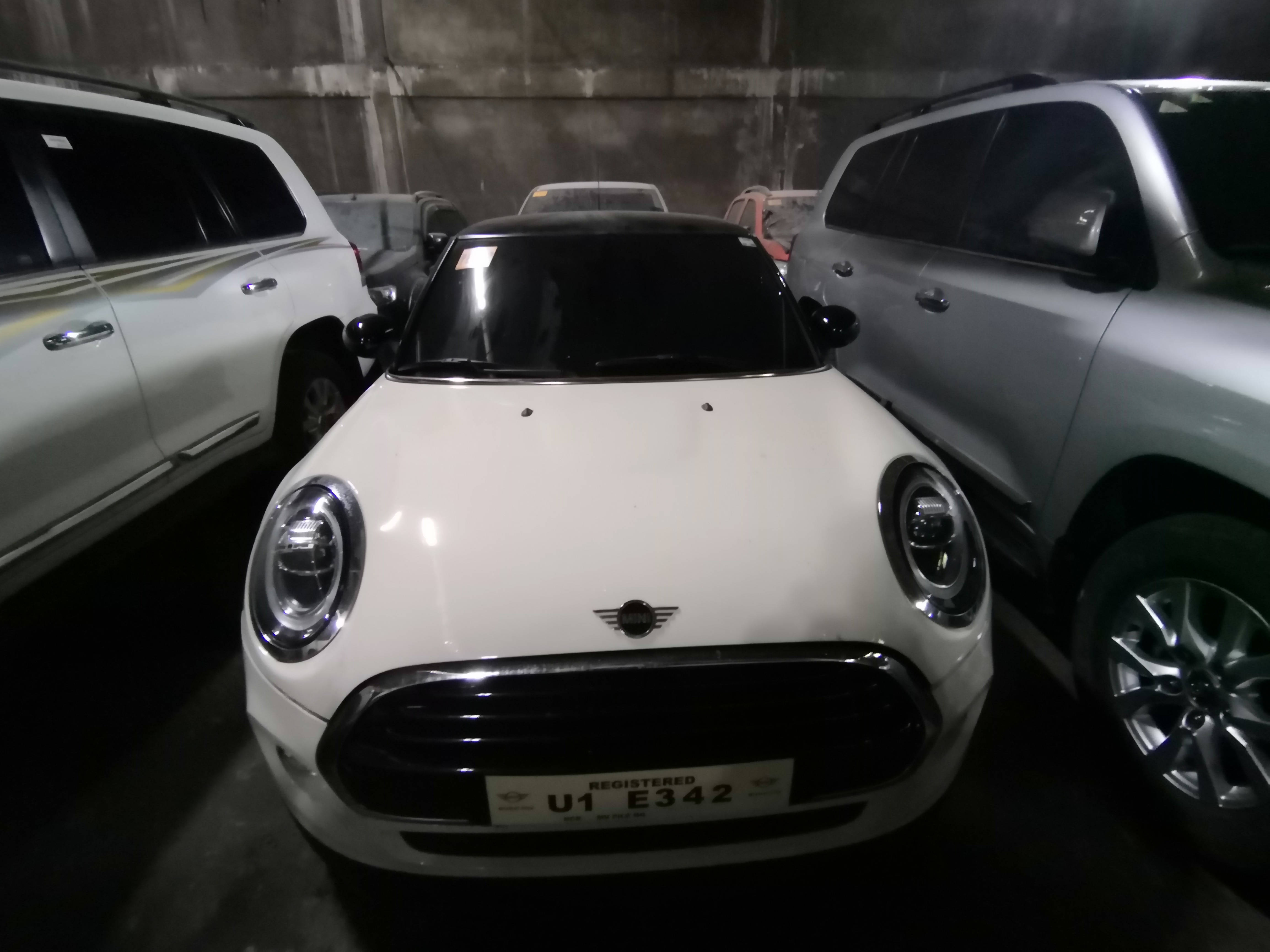 迷你白色車款夾在兩輛灰車之間 壁紙 — 一輛白色Mini Cooper停泊在燈光昏暗的地下停車場，周圍有其他車輛。