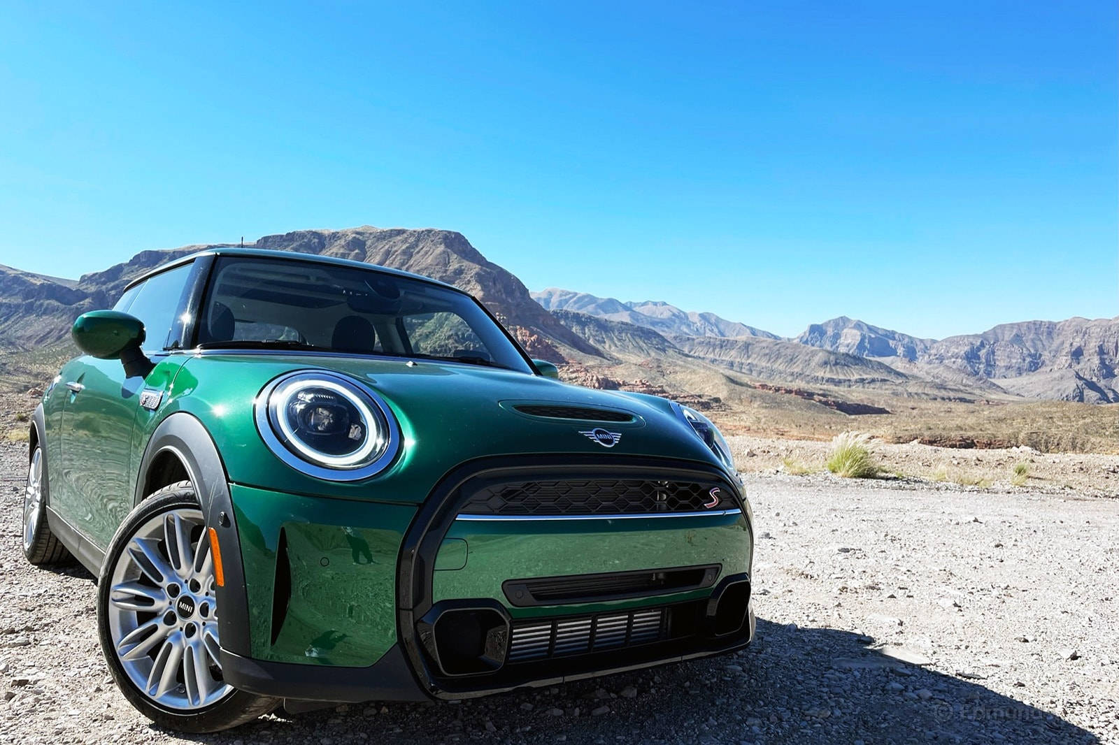 迷你綠色美學沙漠風景 壁紙 — 一輛充滿活力的綠色MINI Cooper S停泊在陽光明媚的沙漠碎石路上，背景是崎嶇的山脈和清澈的藍天。