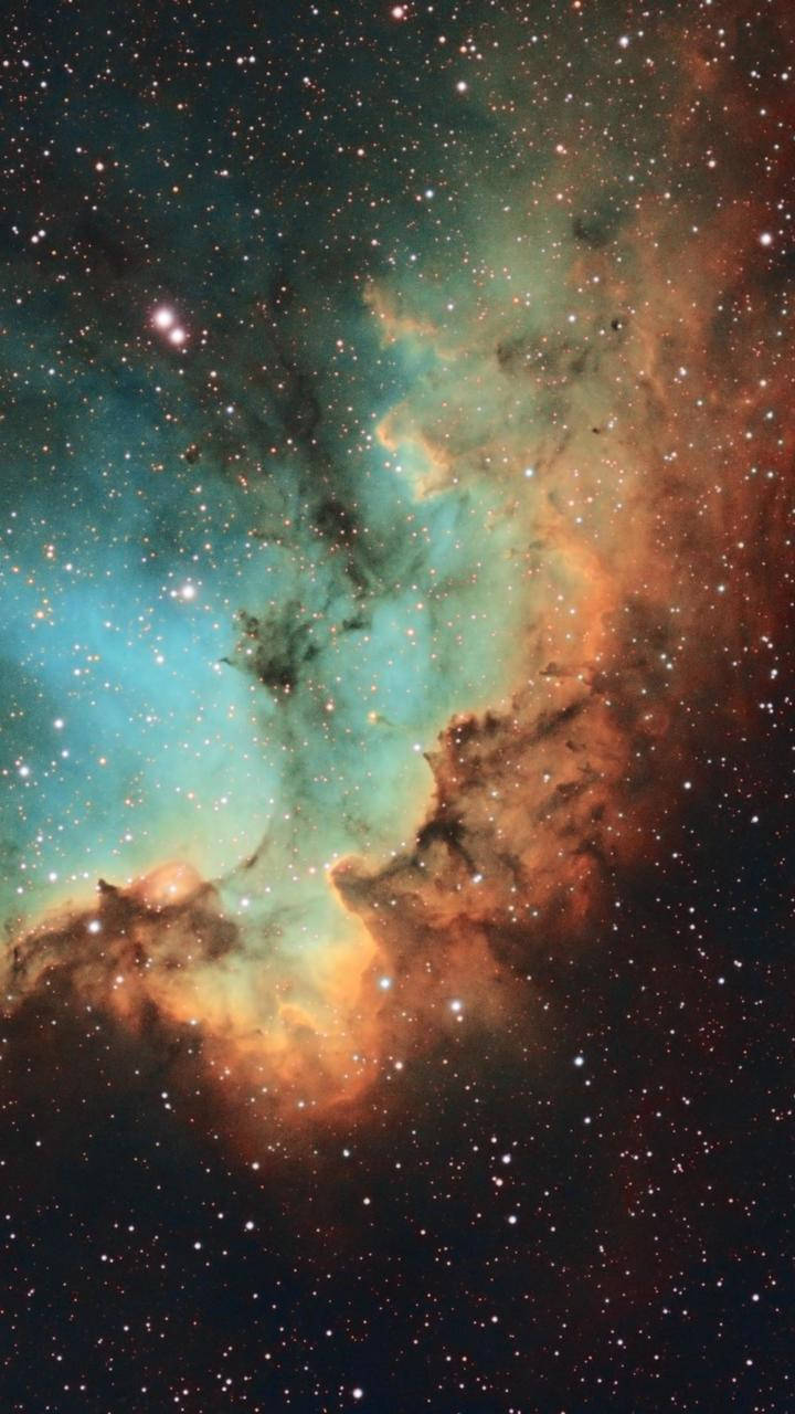 在深空中，鮮豔的青綠色和橙色星雲與星星一起發光。