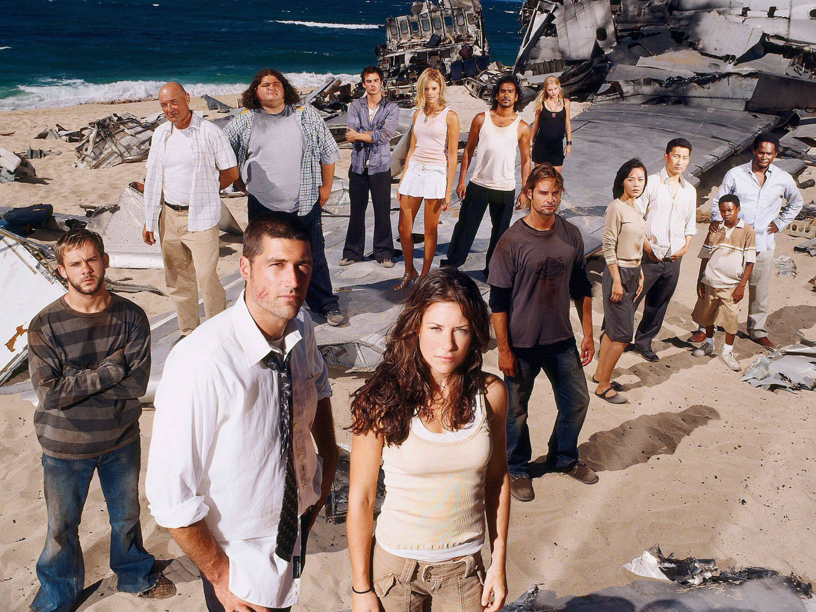 Cast of Lost 站在海灘上，有飛機殘骸和海浪。