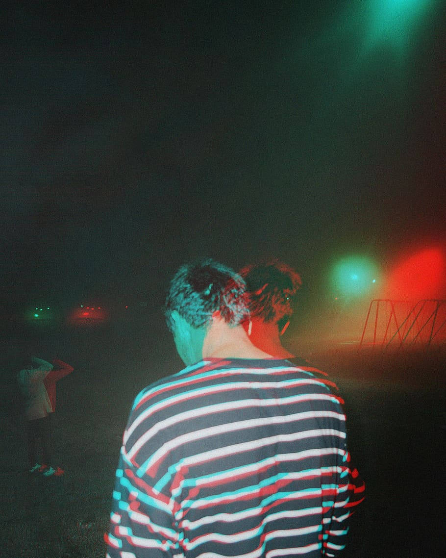 迷幻人物 壁紙 — 一個穿著條紋襯衫的人背對鏡頭，在夜間音樂會中站在色彩繽紛的舞台燈光下。