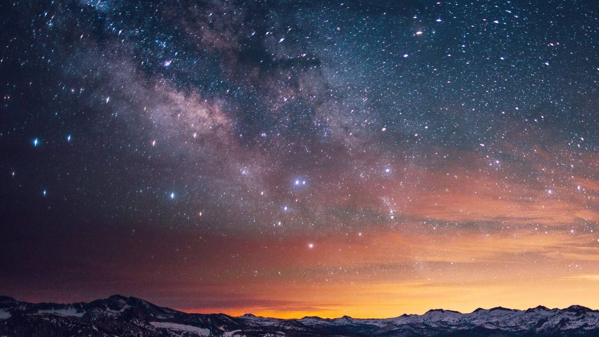 迷幻星夜天際 壁紙 — 令人嘆為觀止的夜空，滿天繁星和銀河在暮色中拱起於積雪覆蓋的山脈之上。