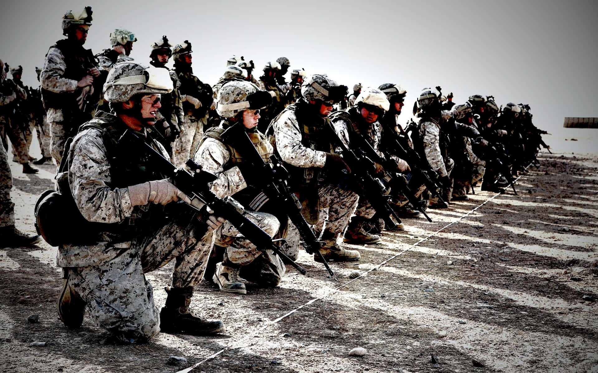 一排跪著的沙漠迷彩士兵在沙地上手持步槍。