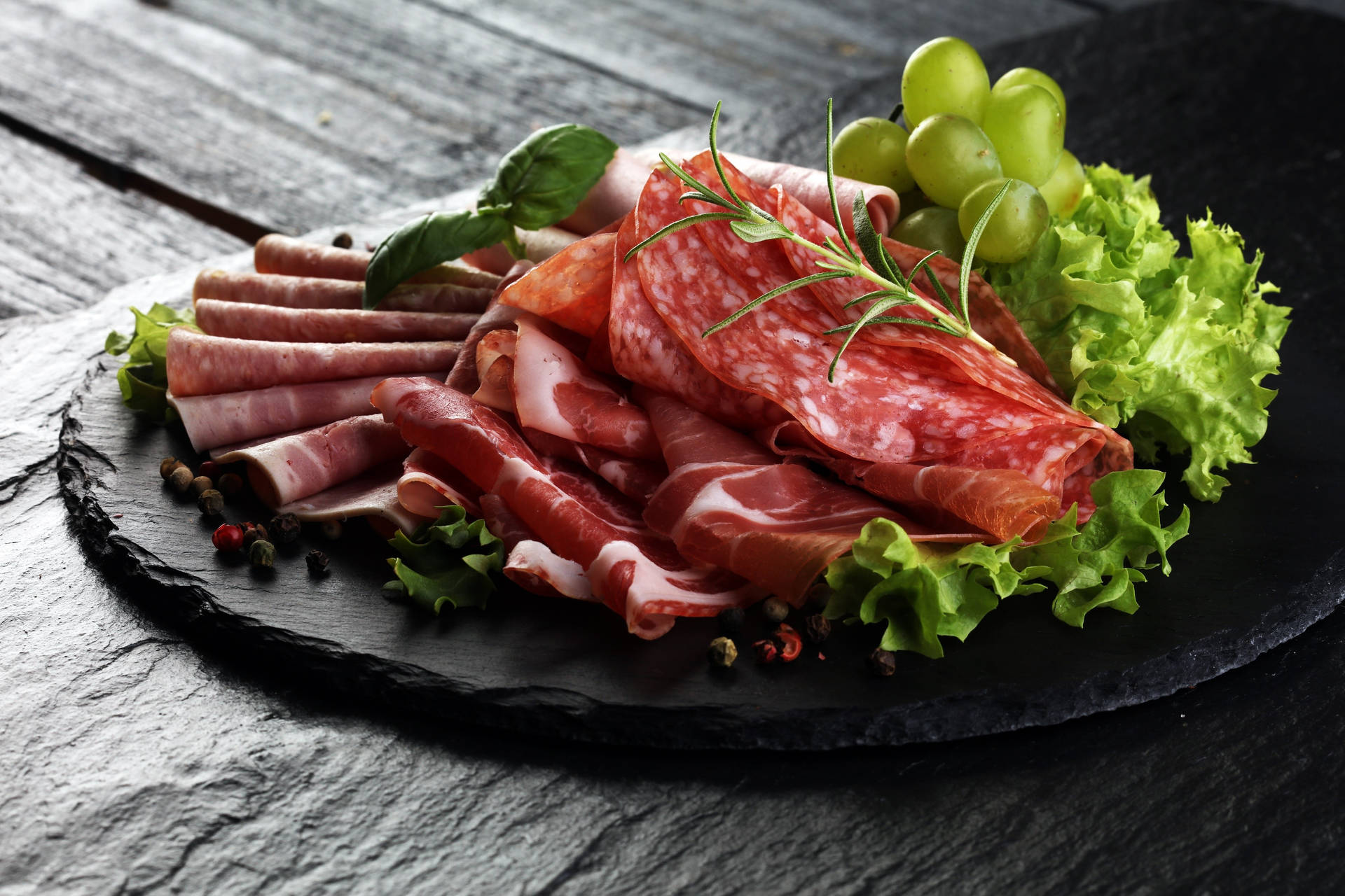 深色石板上的醃製肉類、葡萄、生菜和香草拼盤