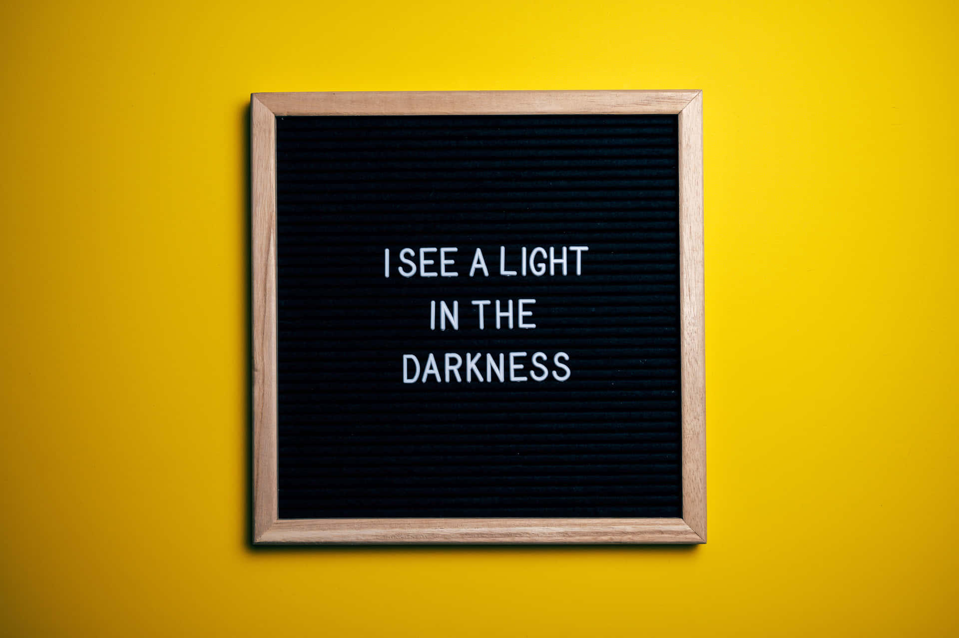 一個帶框的字母板，上面有訊息「I SEE A LIGHT IN THE DARKNESS」在黃色牆上。