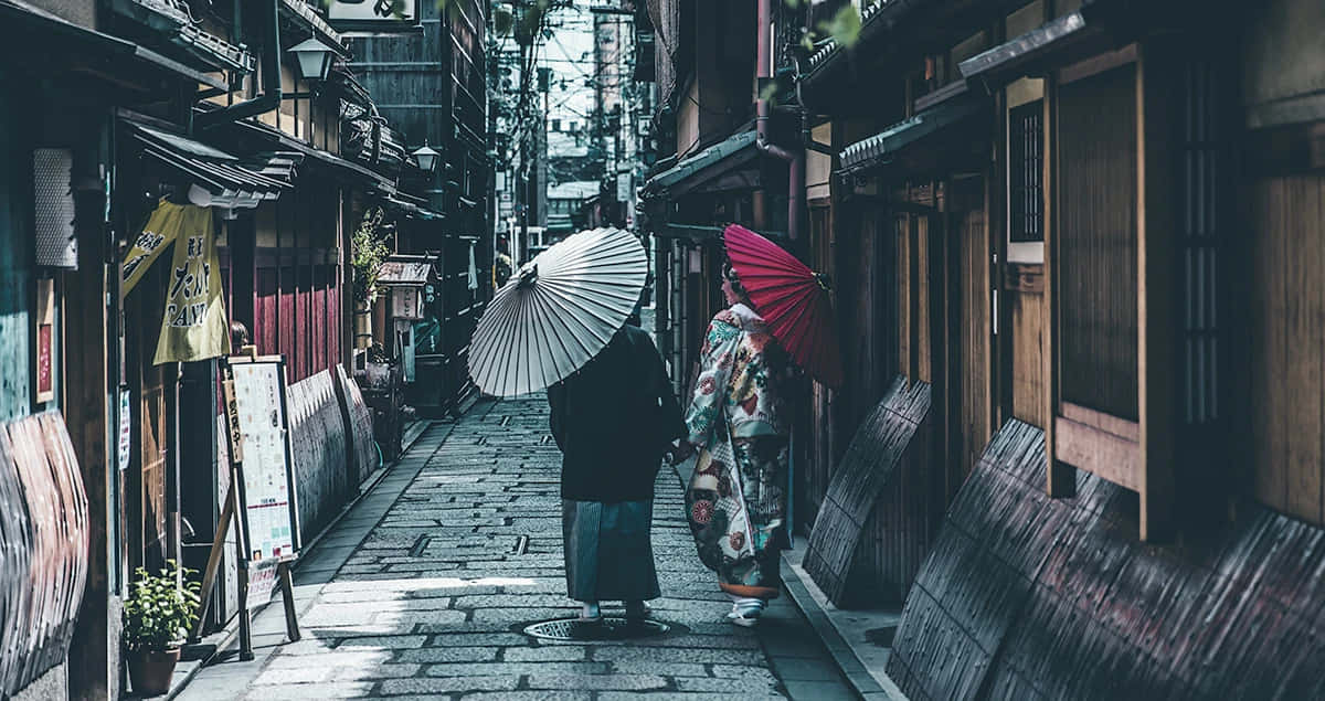兩個穿著傳統日本服裝的人，沿著一條有木建築的狹窄石巷走著。