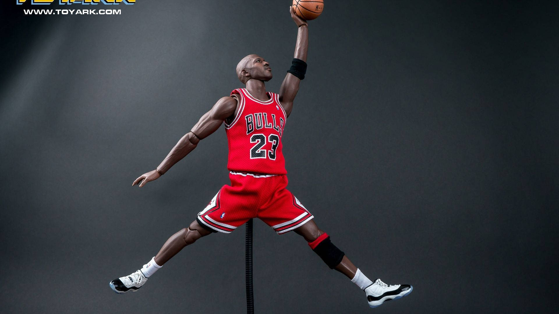 追求卓越——邁克爾·喬丹 壁紙 — 一個細節豐富的Michael Jordan動作人偶，身穿標誌性紅色公牛隊球衣，在黑暗工作室背景下空中灌籃。