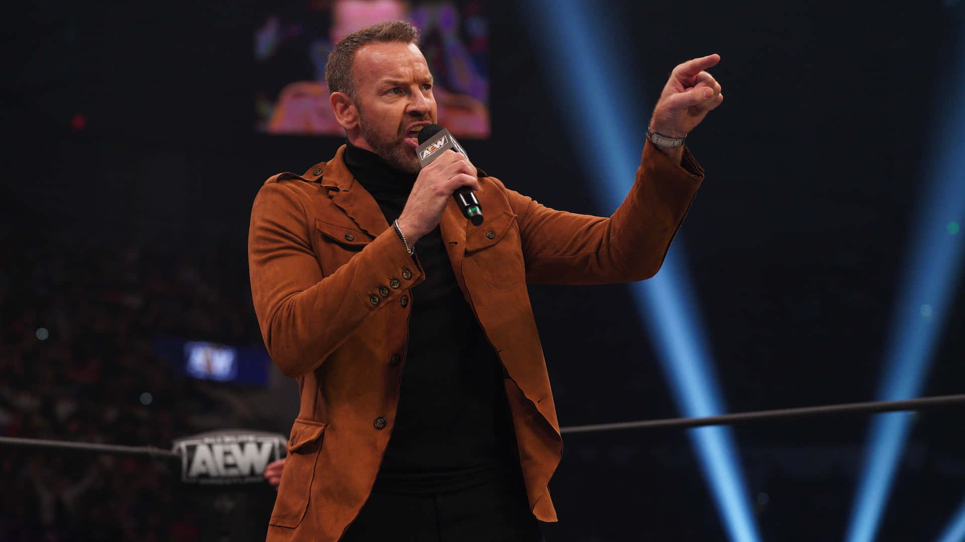 AEW 賽事中，摔角手在藍光下於擂台內對著麥克風說話。