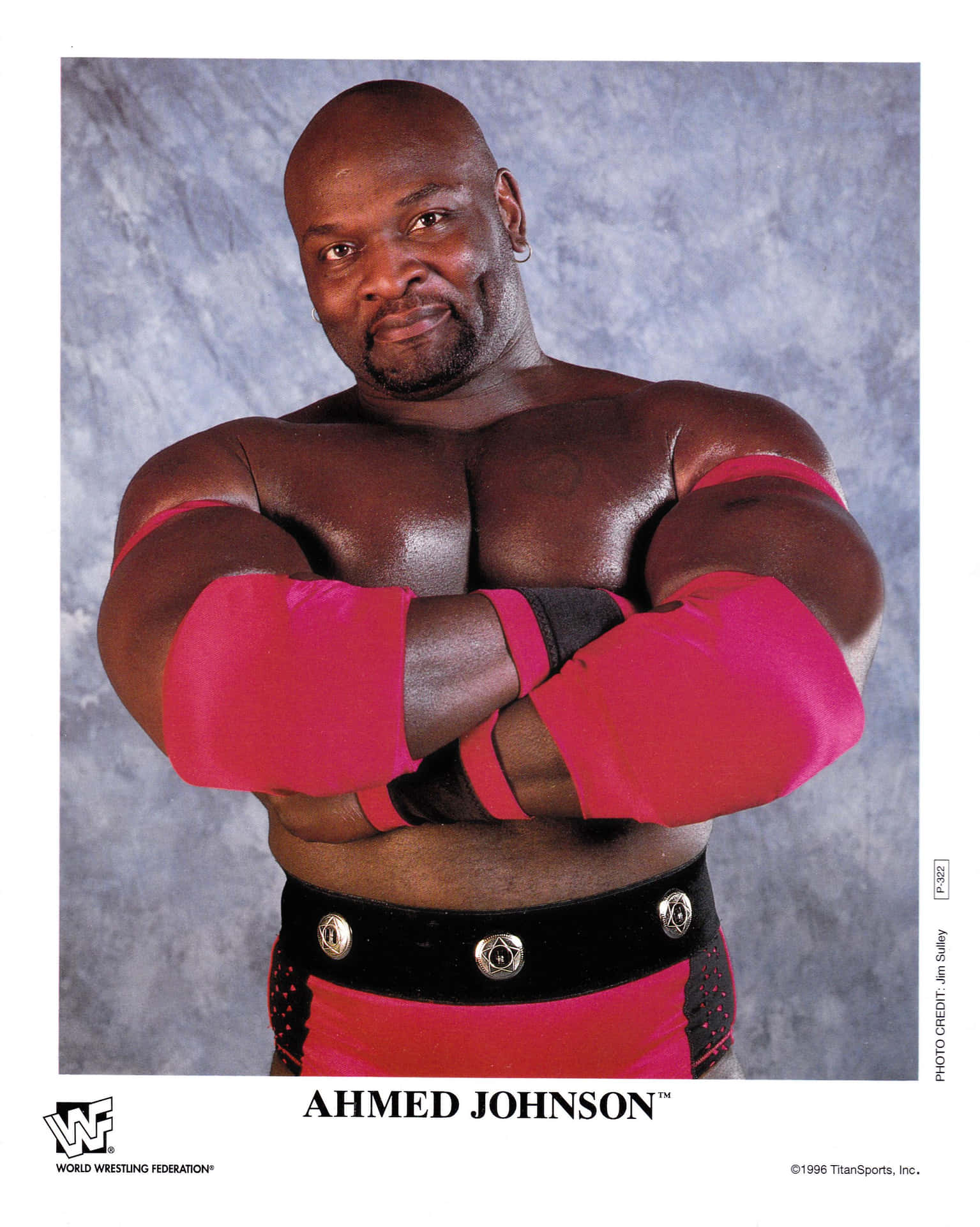 退役摔跤手阿赫邁德·約翰遜 壁紙 — 肌肉發達的摔角手 Ahmed Johnson 在紋理灰色背景前自信地交叉雙臂擺姿勢。
