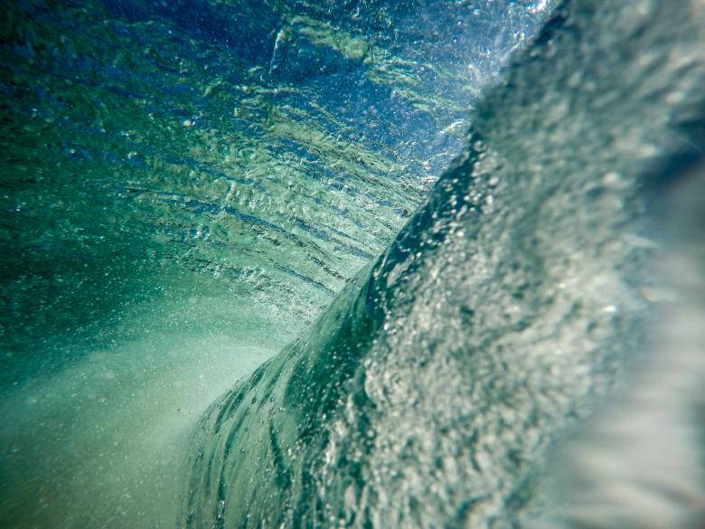 藍綠色海浪在水下破碎，帶有氣泡和陽光。