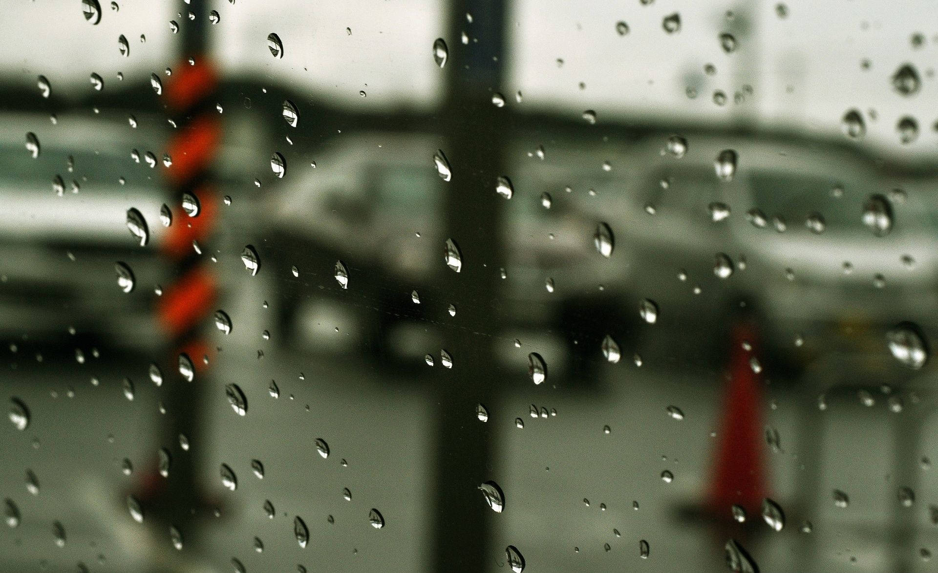 窗戶上的雨滴，俯瞰一條模糊的街道，有汽車和橙色錐體。