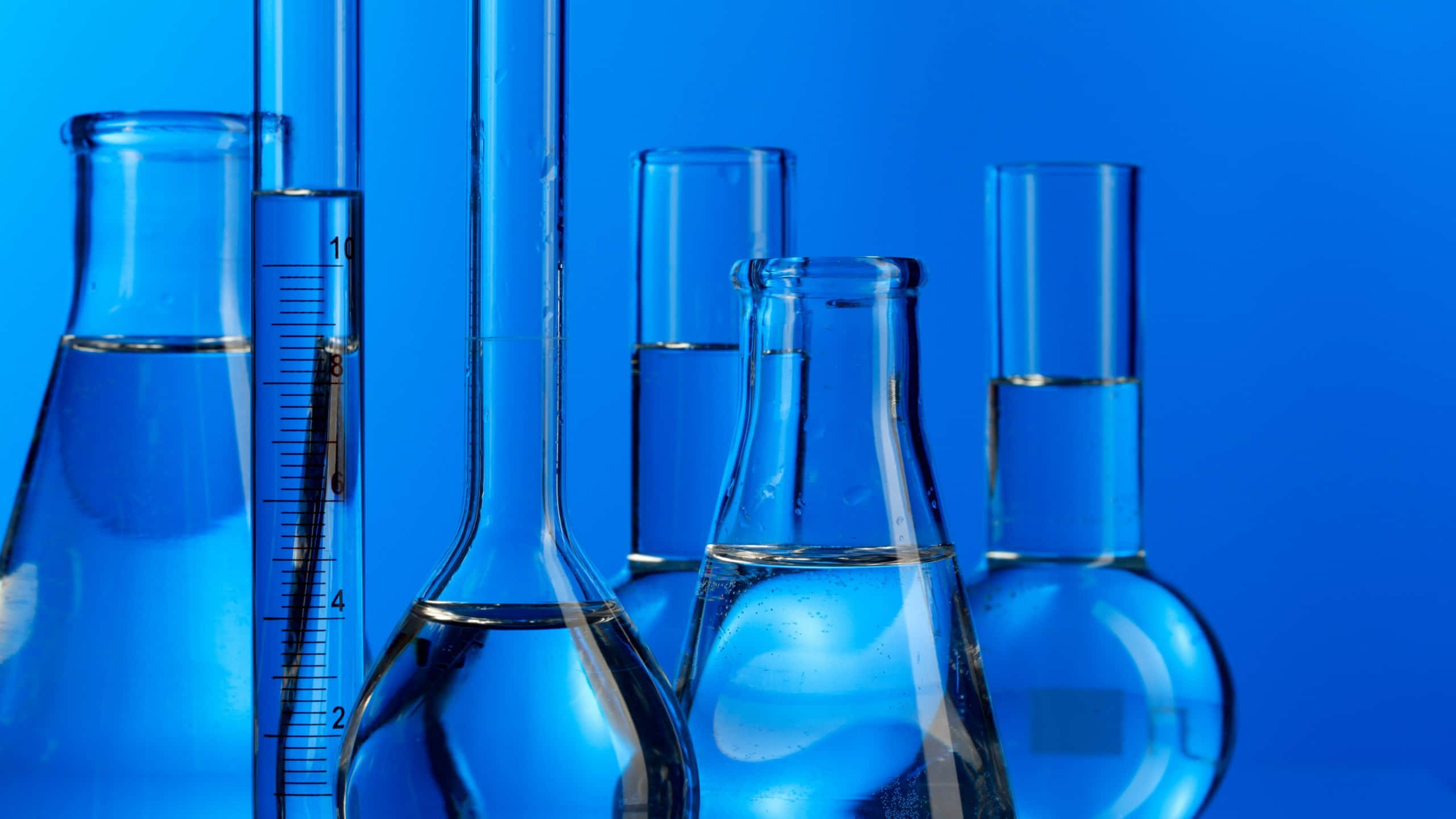 Chemistry 桌布 壁紙 — 透明玻璃燒瓶和試管裝滿液體，矗立在鮮豔的藍色背景前。