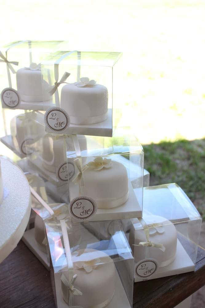 堆疊的白色迷你結婚蛋糕，放在透明盒子中，附有字母組合標籤，置於木桌上。