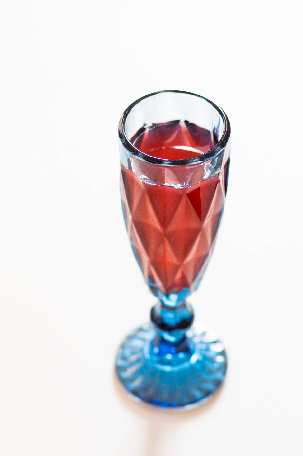 白色表面上一個帶有紅色液體的藍色切面玻璃杯。