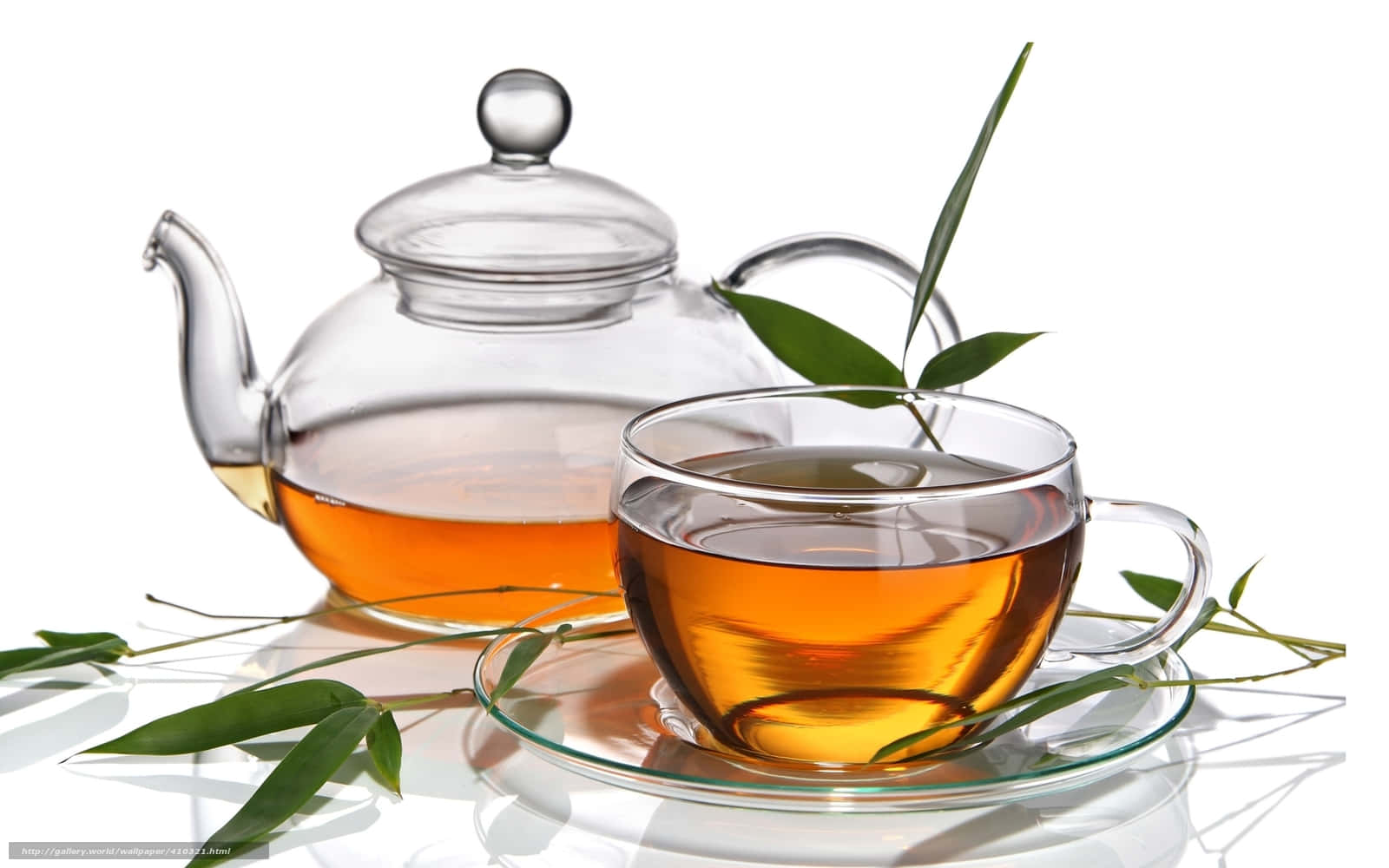 透明茶杯與茶壺圖 壁紙 — 一個透明玻璃茶壺和杯子，裝滿琥珀色茶，周圍是新鮮的綠色竹葉，放在白色反光表面上。