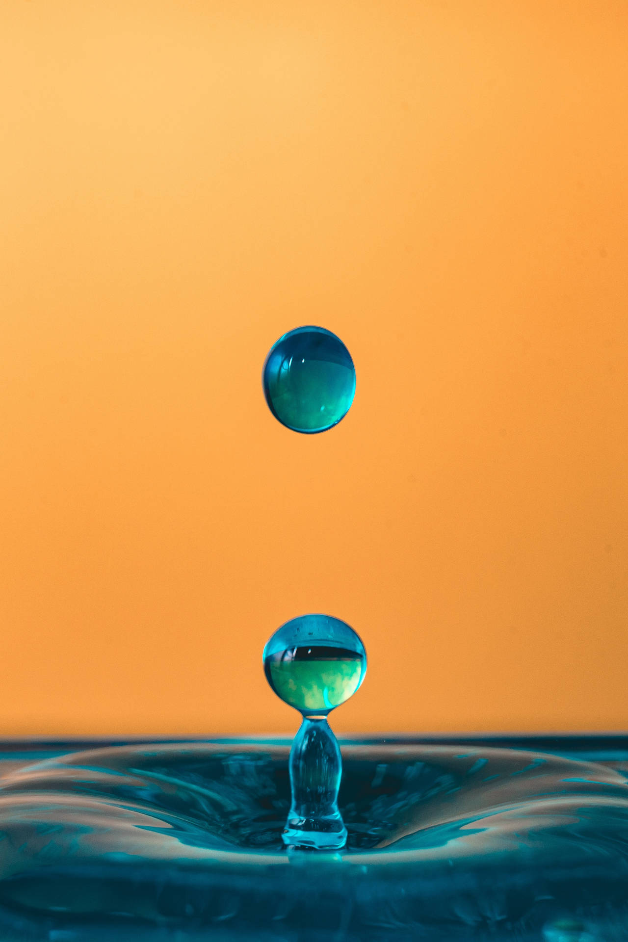 藍色水滴懸浮在空中，在漣漪表面之上，背景為橙色。
