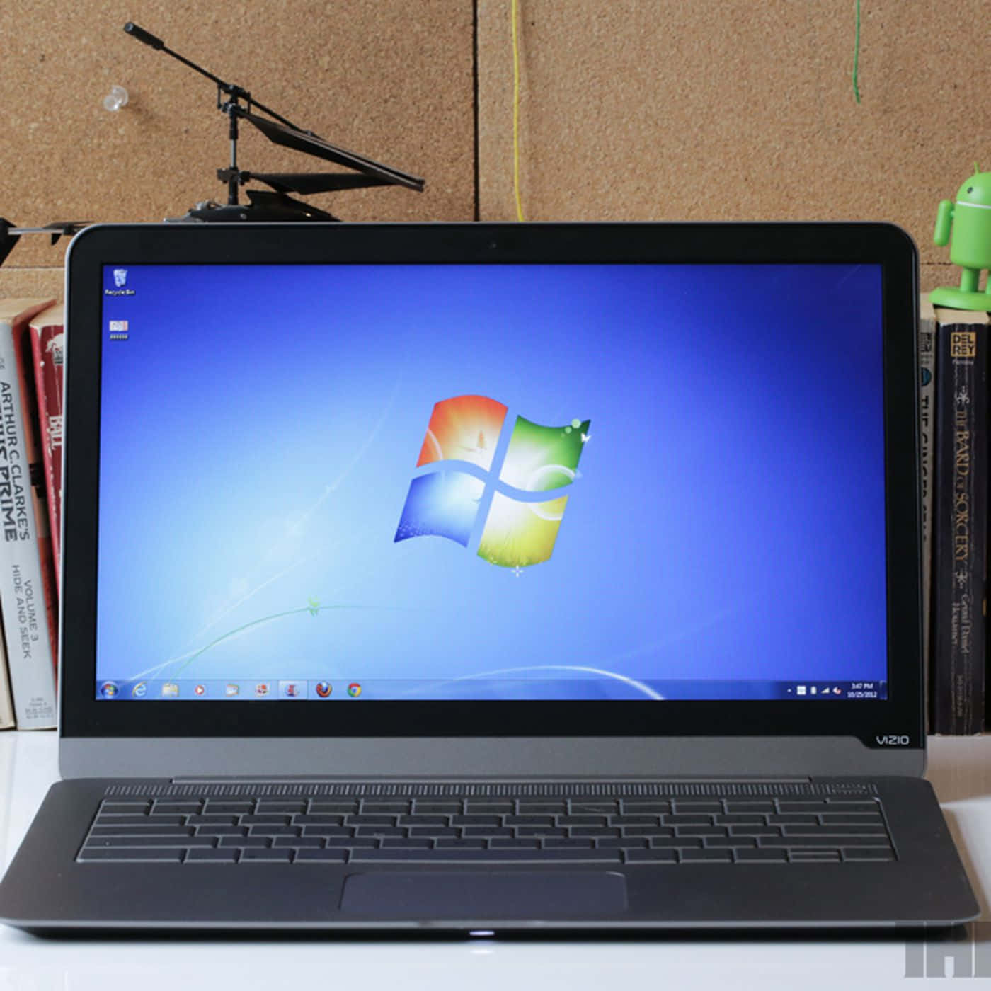 黑色手提電腦顯示Windows 7桌面，附近有書本和Android公仔。