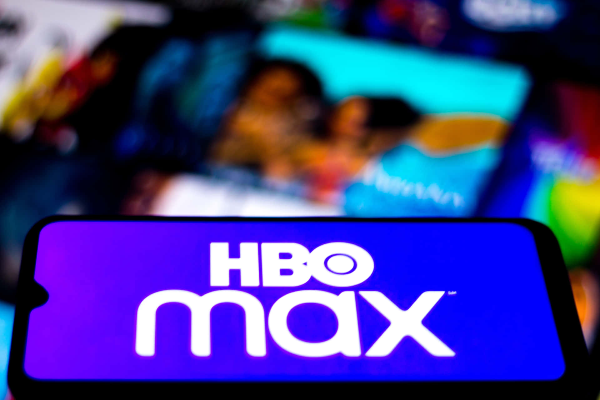手機特寫，顯示HBO Max應用程式標誌，背後有模糊的串流內容。