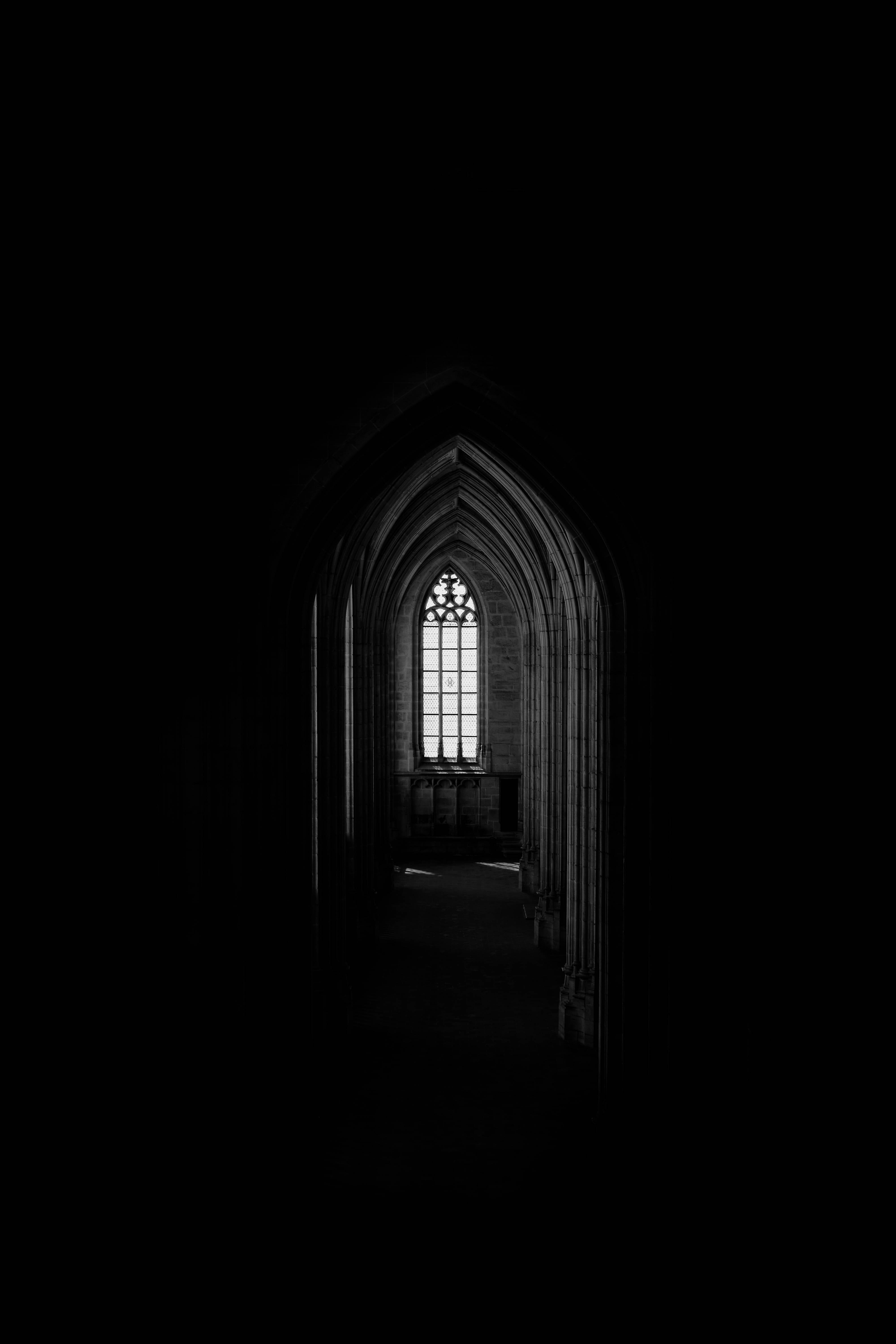 simple dark aesthetic 桌布 壁紙 — 透過哥德式拱門望向光線昏暗的大教堂走廊，盡頭是發光的彩繪玻璃窗，呈現鮮明的黑白景觀。