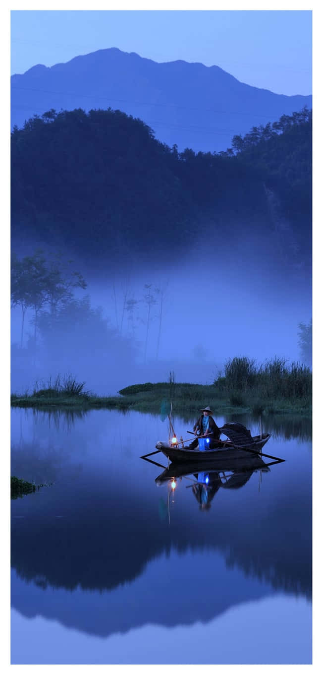 漁夫在霧湖上暮色中划船，山巒倒影