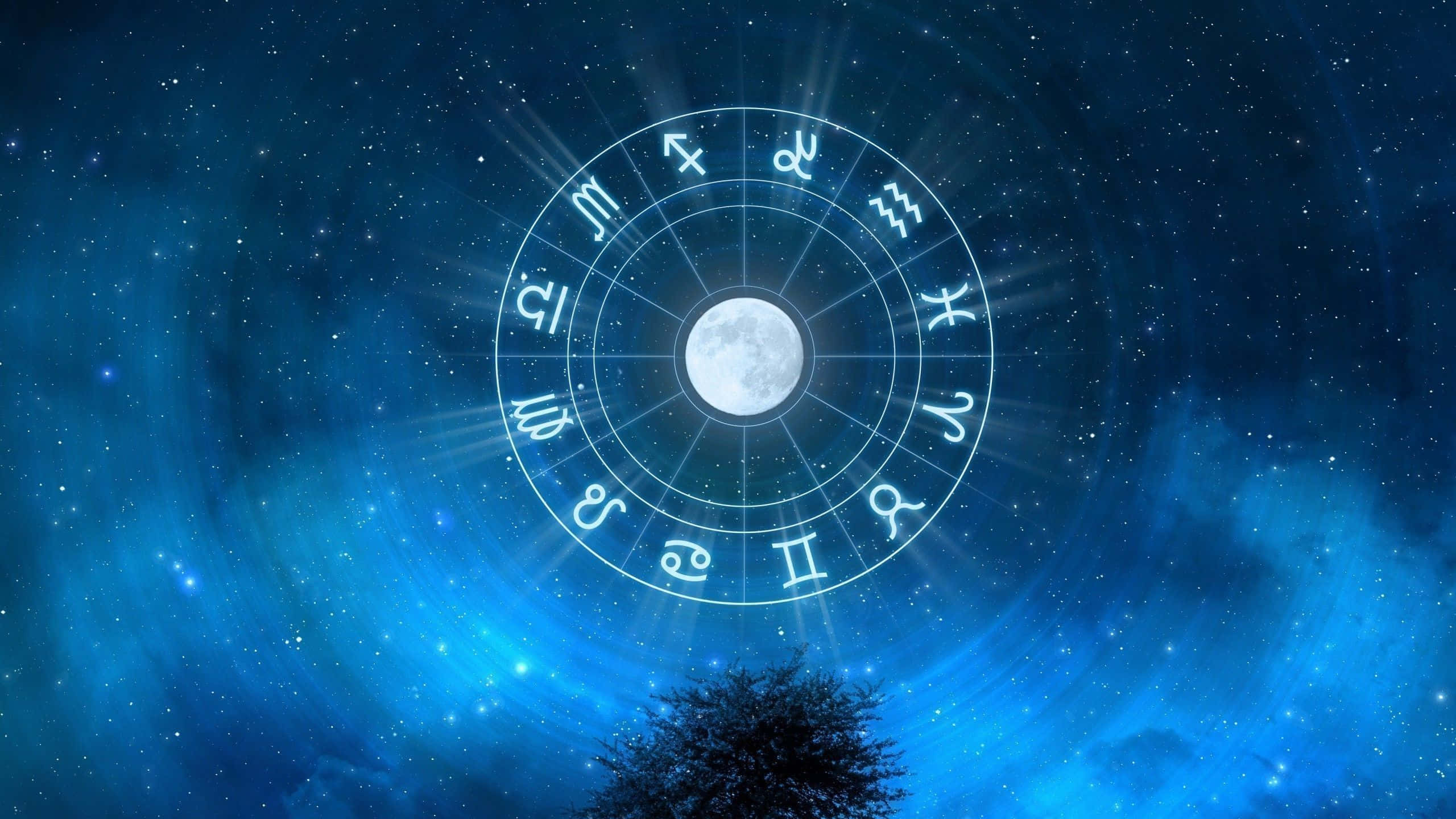透過星象學揭開宇宙奧秘 壁紙 — 一個發光的黃道輪，中心有月亮，漂浮在一棵樹上方，背景是繁星點點的藍色夜空。