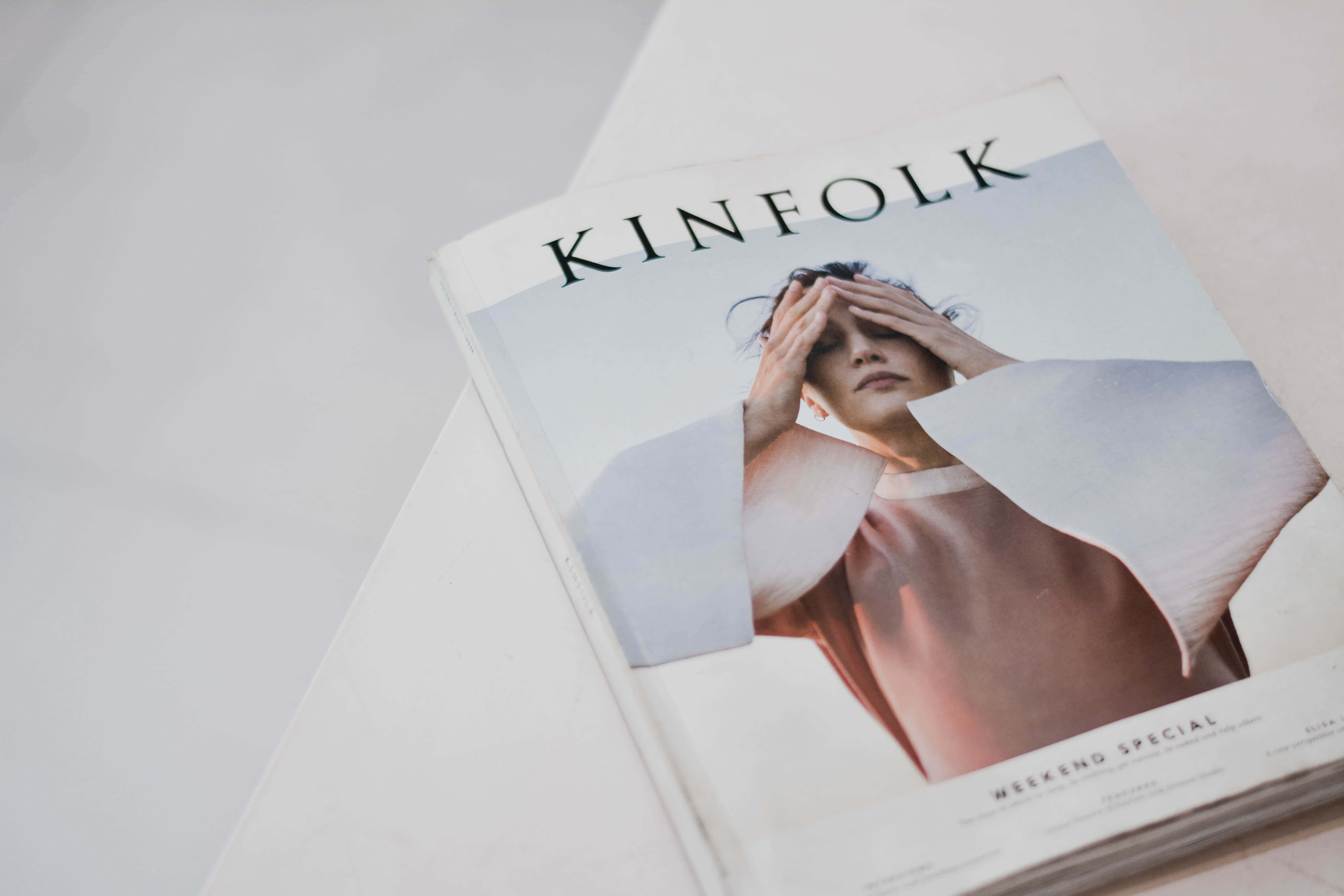 透過最愛雜誌保持資訊更新 壁紙 — Kinfolk雜誌封面的特寫，一名身穿粉紅色上衣的人將手放在眼睛上，擱在白色表面上。