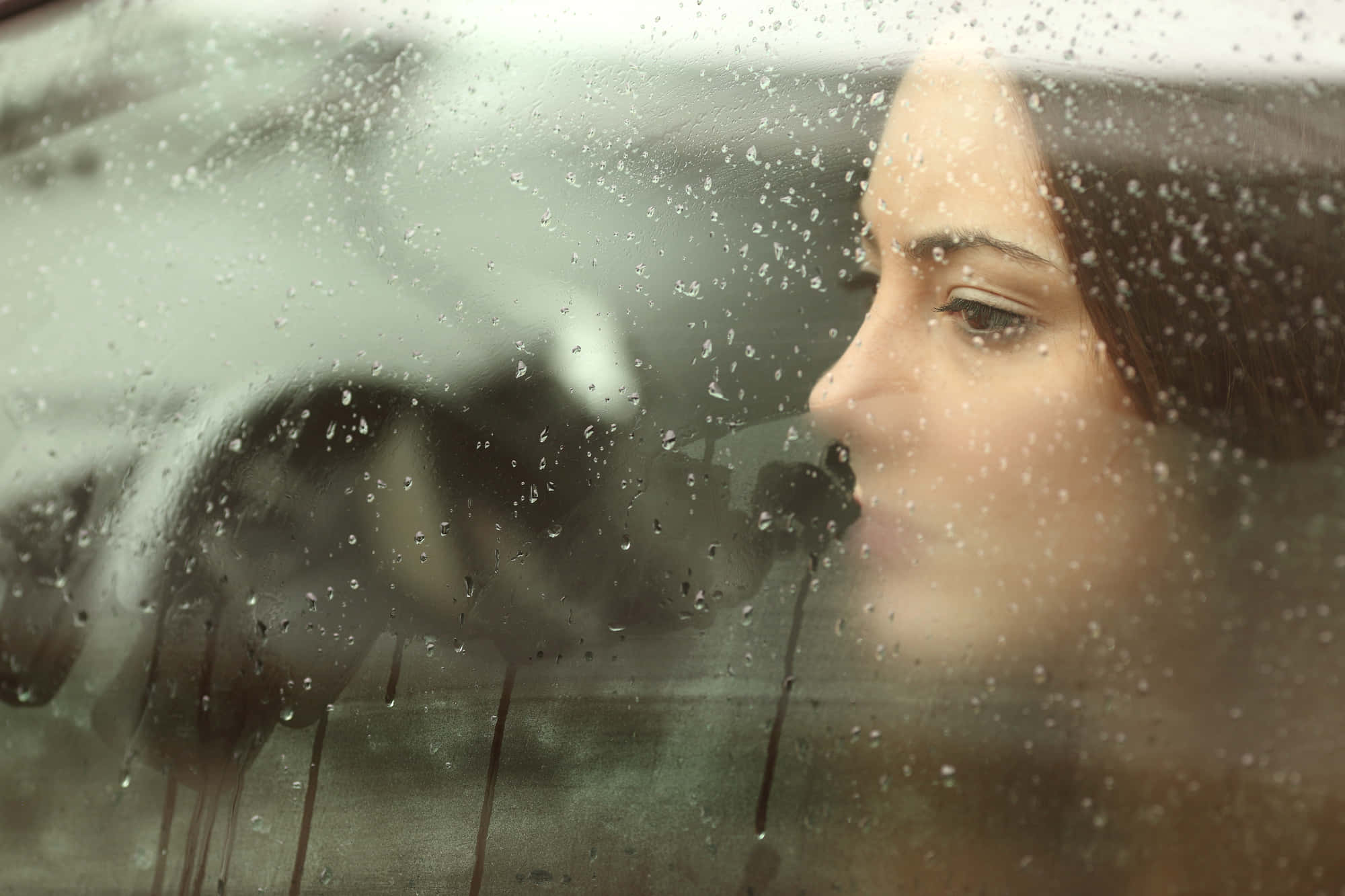 sadness 桌布 壁紙 — 透過沾滿雨點的車窗看到的女性沉思側面，背景模糊。