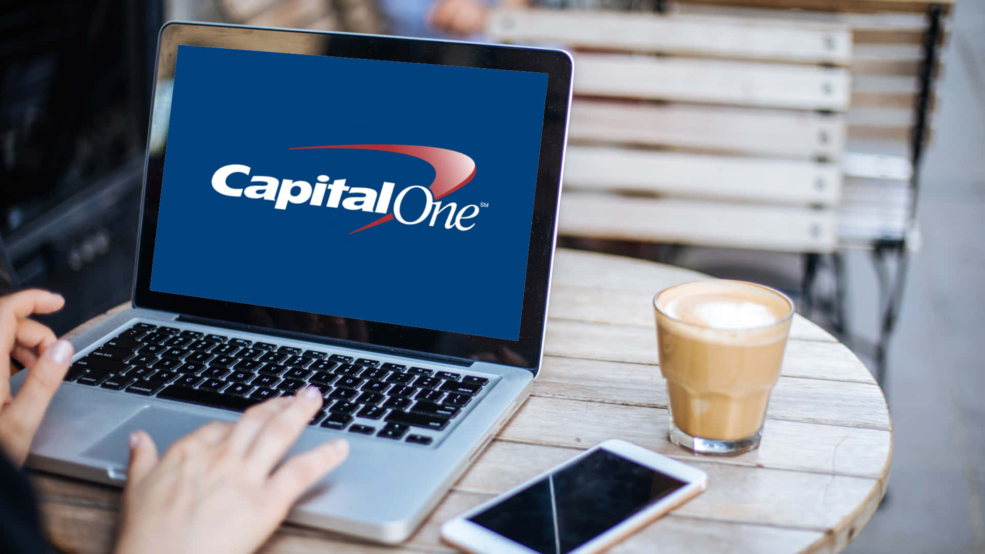 在咖啡桌旁使用帶有Capital One標誌的筆記型電腦，旁邊有咖啡和手機。