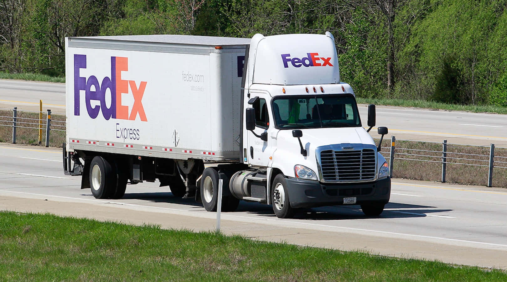 FedEx貨車在陽光明媚的高速公路上行駛，周圍有綠樹和草地。