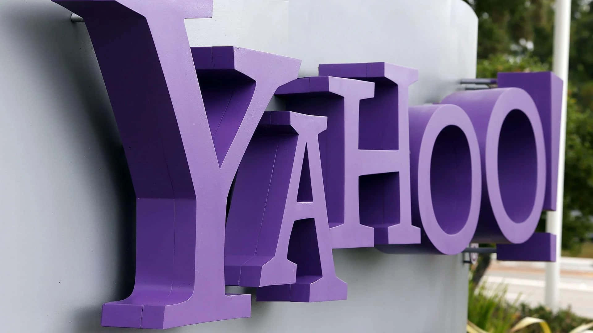 灰色建築物上的紫色 Yahoo 標誌，附近有綠色植物。