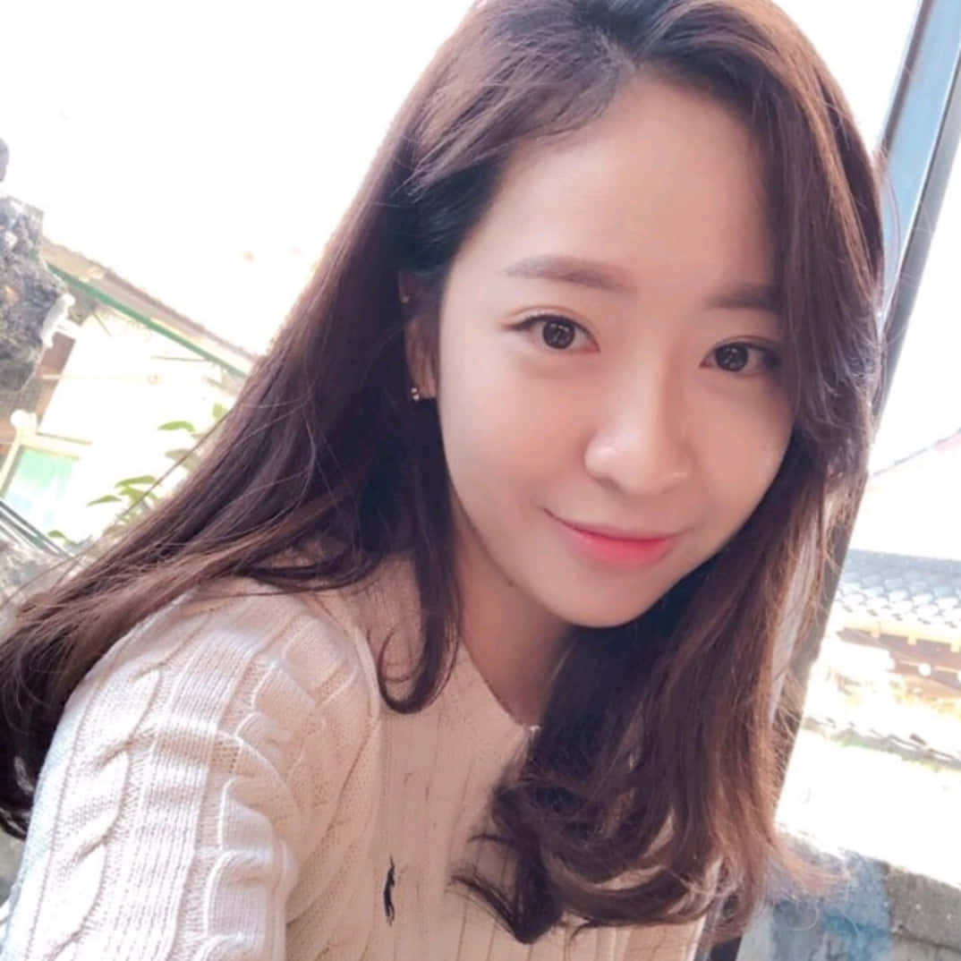 這位可愛女孩的笑容照亮整個房間 壁紙 — 一位留著長長棕色頭髮的年輕女性，穿著奶油色麻花針織毛衣，溫柔地微笑。
