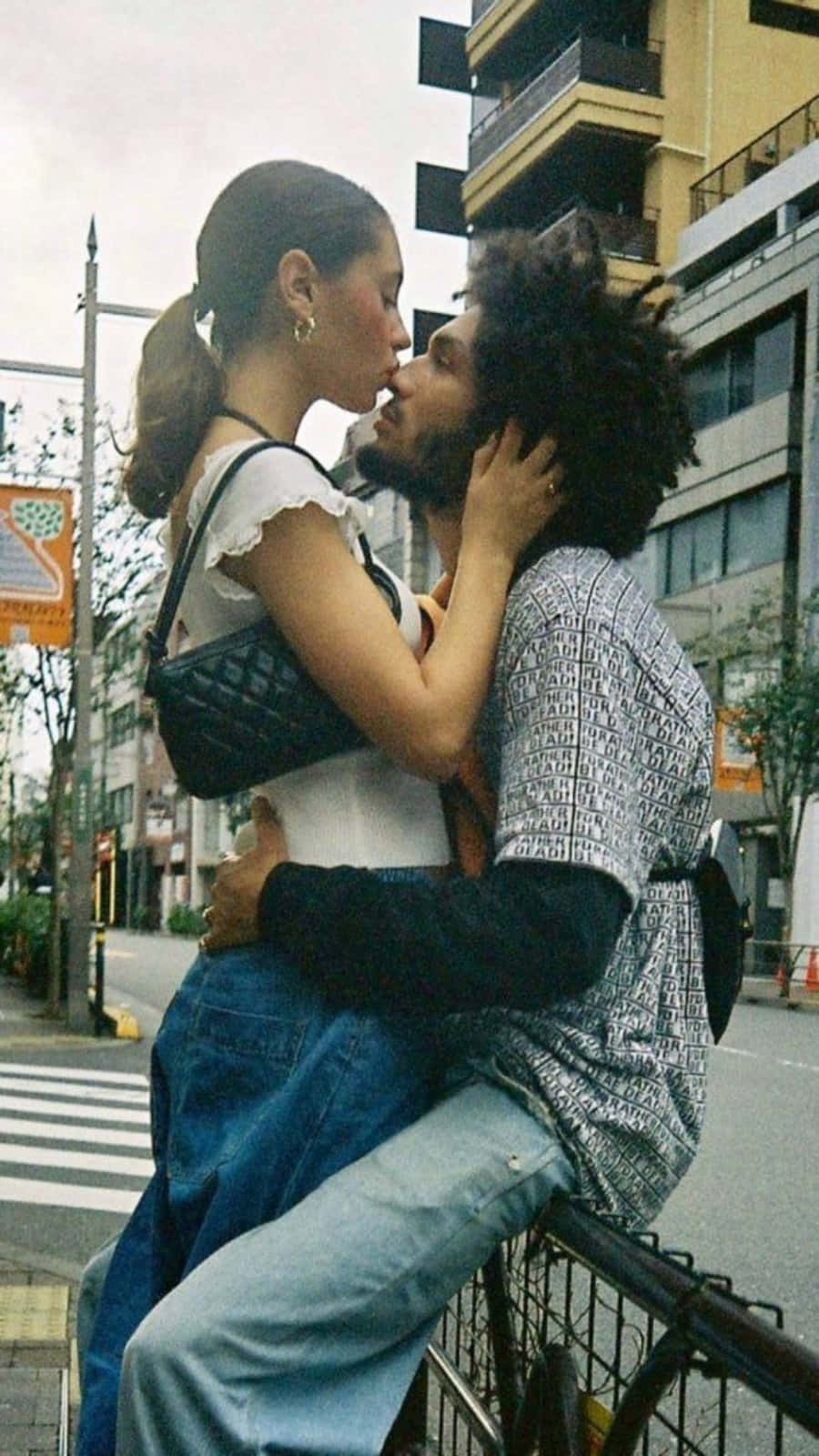 一對情侶在城市的街道上熱情接吻，男子靠在欄杆上。