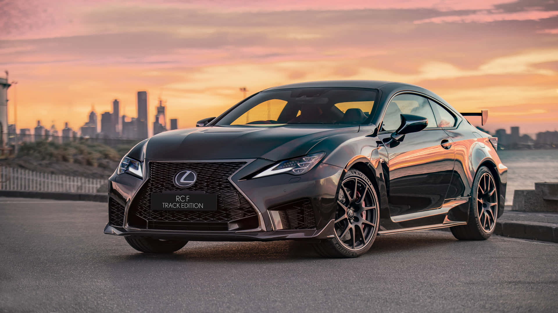 日落時分，黑色Lexus RCF Track Edition停在海濱，背後是城市天際線。