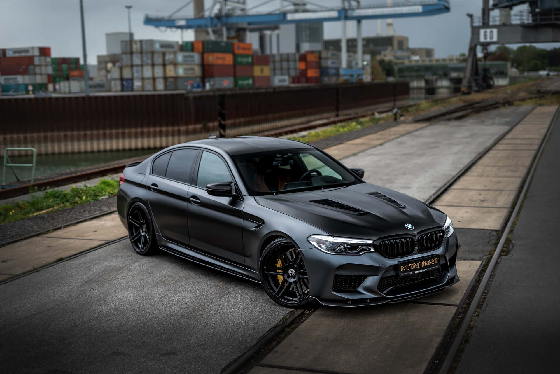 啞光黑色BMW M5停泊在工業港口附近的鐵路軌道旁。