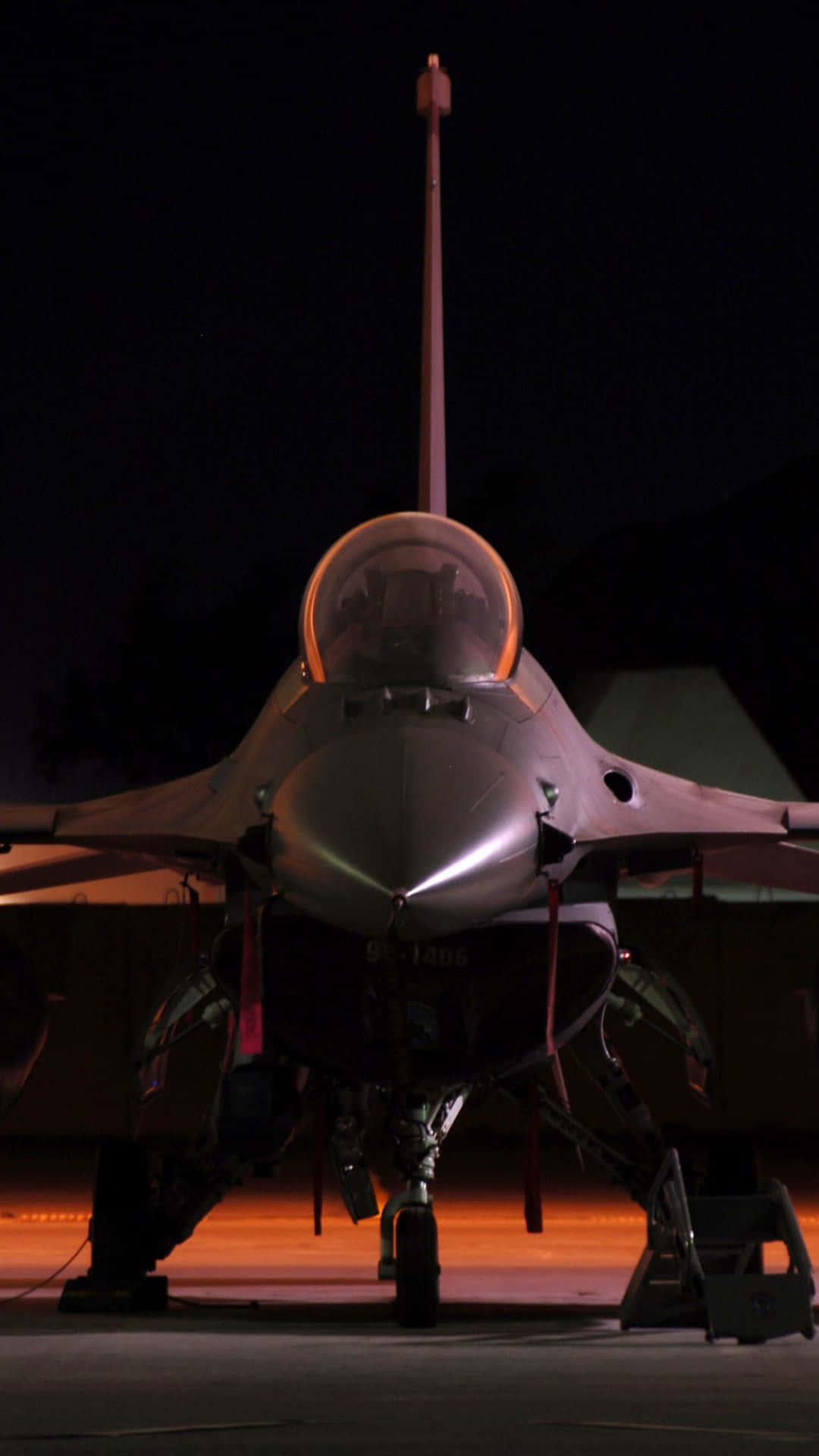 通用動力F-16戰隼安卓巨無霸背景 壁紙 — 一架戰鬥機在夜間停放在停機坪上，在黑暗的天空下被溫暖的橙色地面燈光照亮。