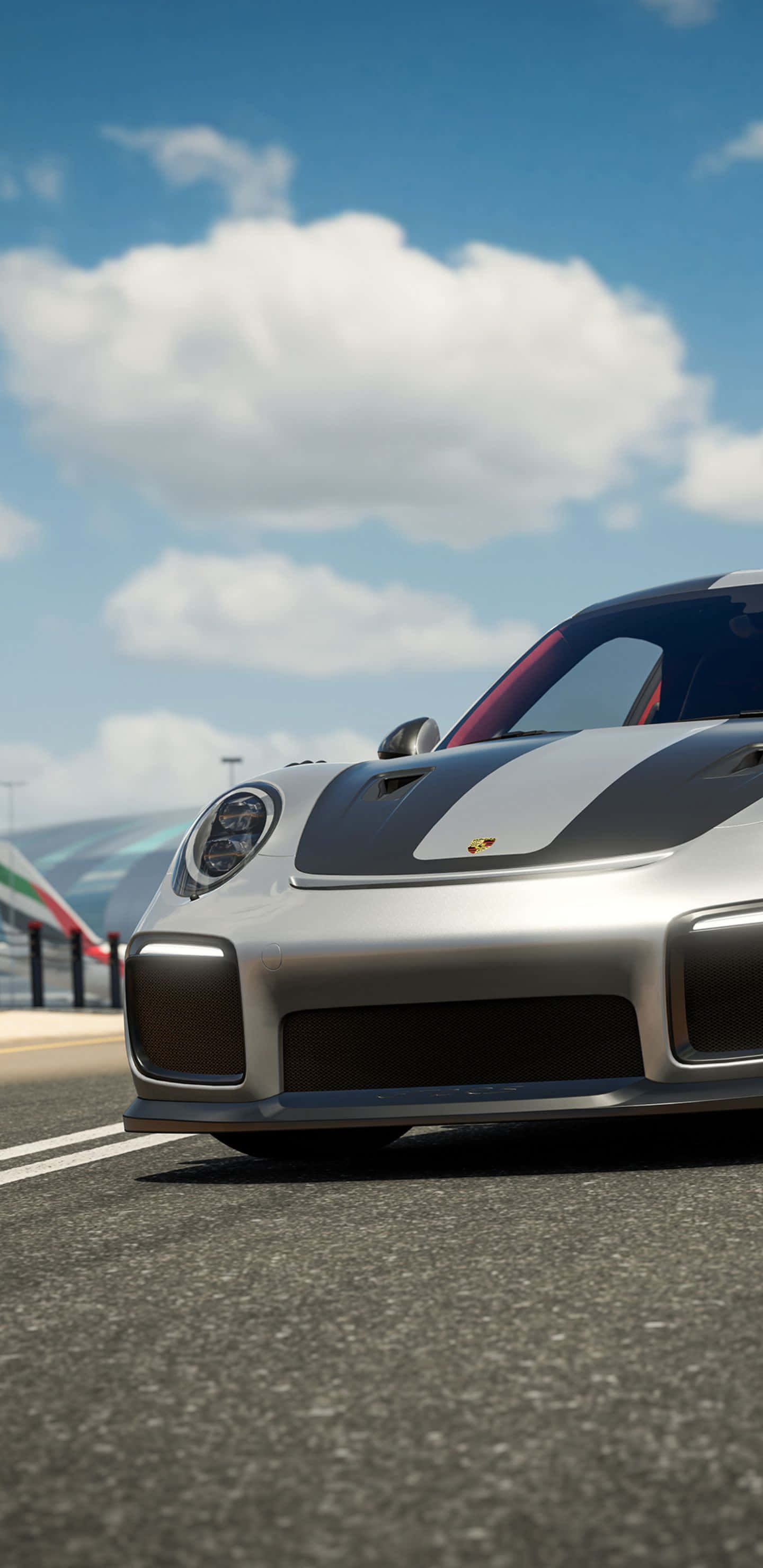 速度、性能與優雅：Forza Motorsport 7 在 Pixel 3XL 上的體驗 壁紙 — 一輛時尚的銀色保時捷跑車帶有黑色賽車條紋，在晴朗藍天和蓬鬆白雲下沿著賽道飛馳。