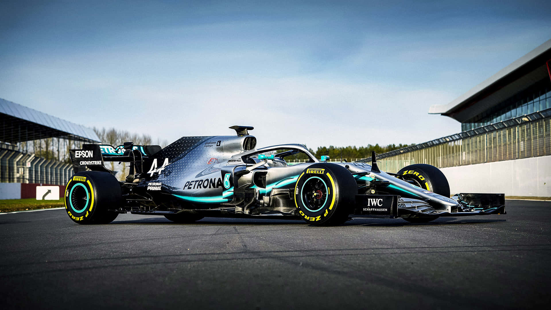 速度、策略與技巧在F1賽車世界中完美結合 壁紙 — 一架時尚的銀色和青綠色一級方程式賽車，編號44，停泊在賽道上，天空湛藍清澈。