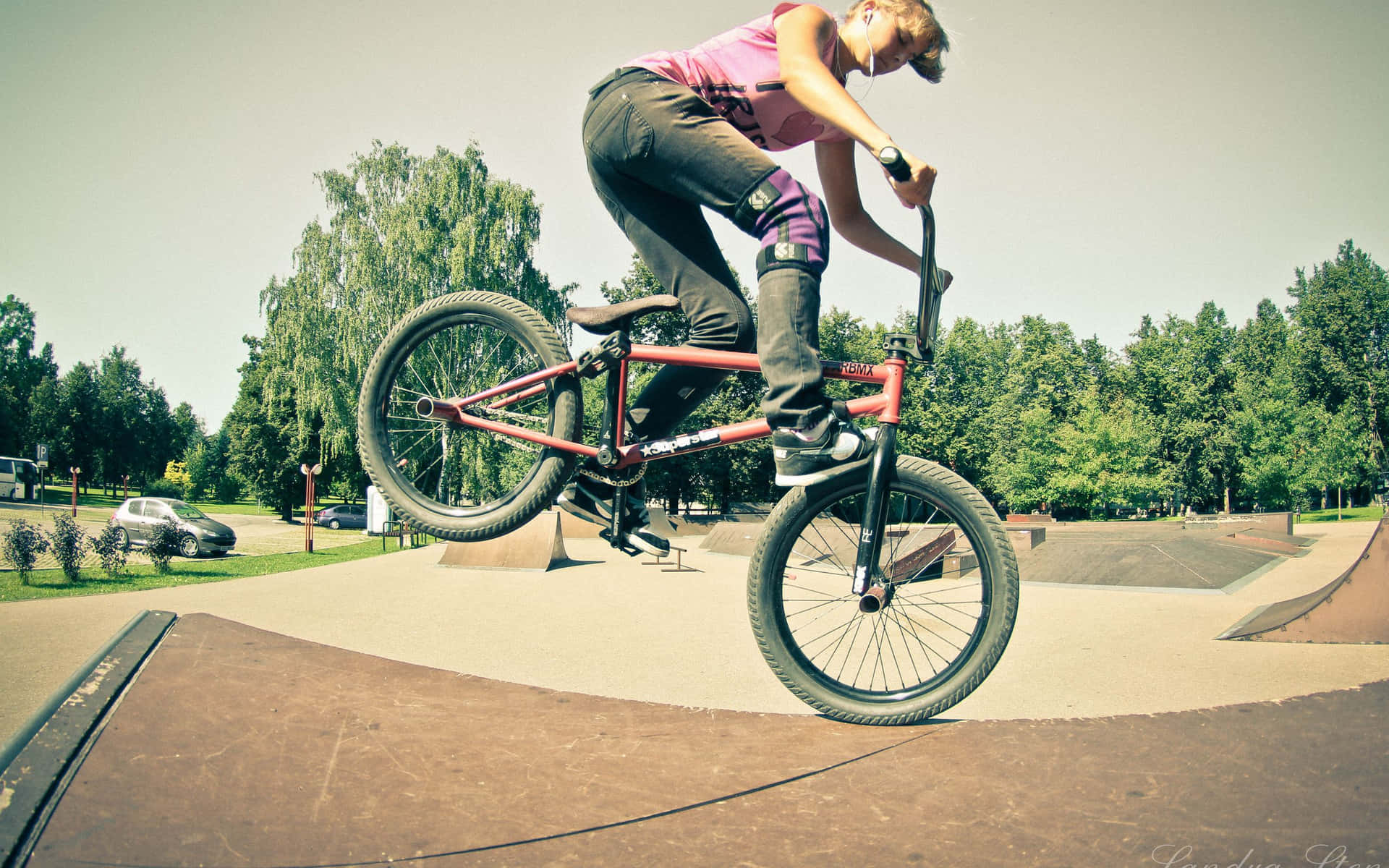 BMX車手在滑板公園騎紅色單車騰空，背景有樹木。