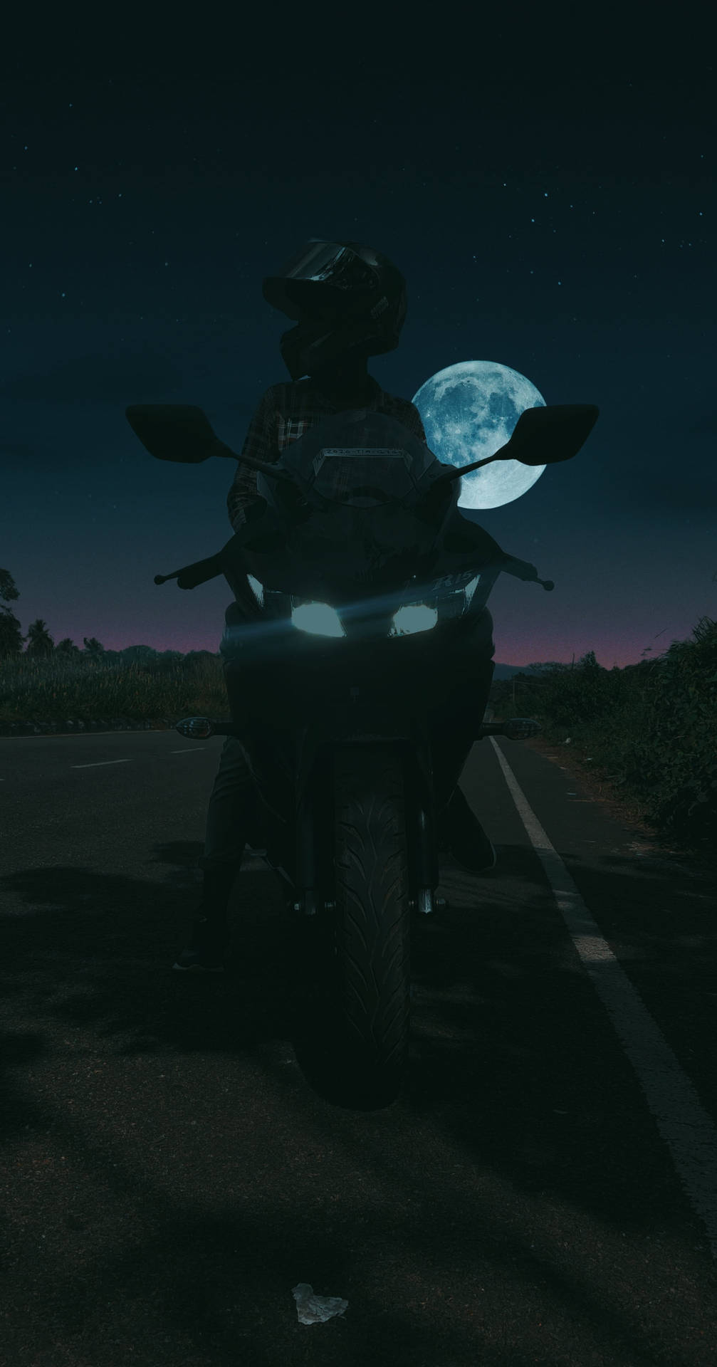 電單車手在滿月下夜間行駛在安靜的道路上。