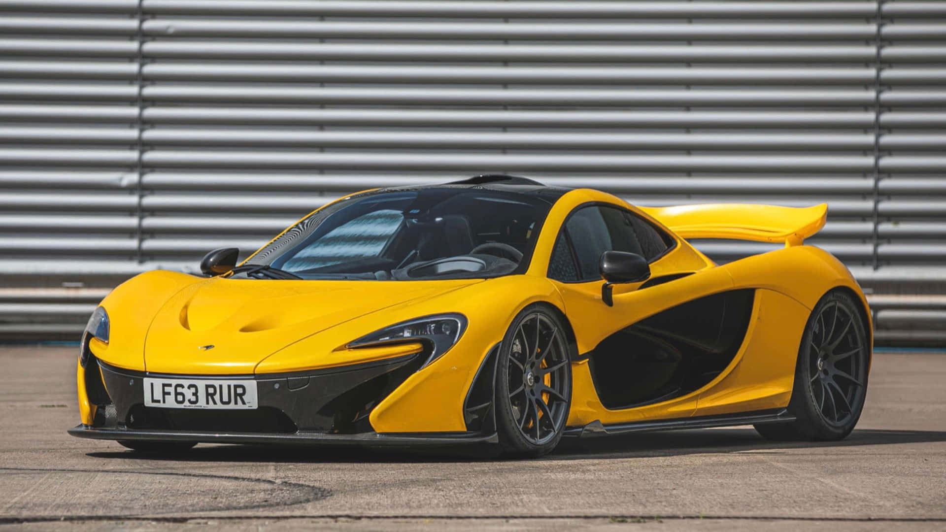 黃色McLaren P1超級跑車在賽道上，背景為金屬護欄。