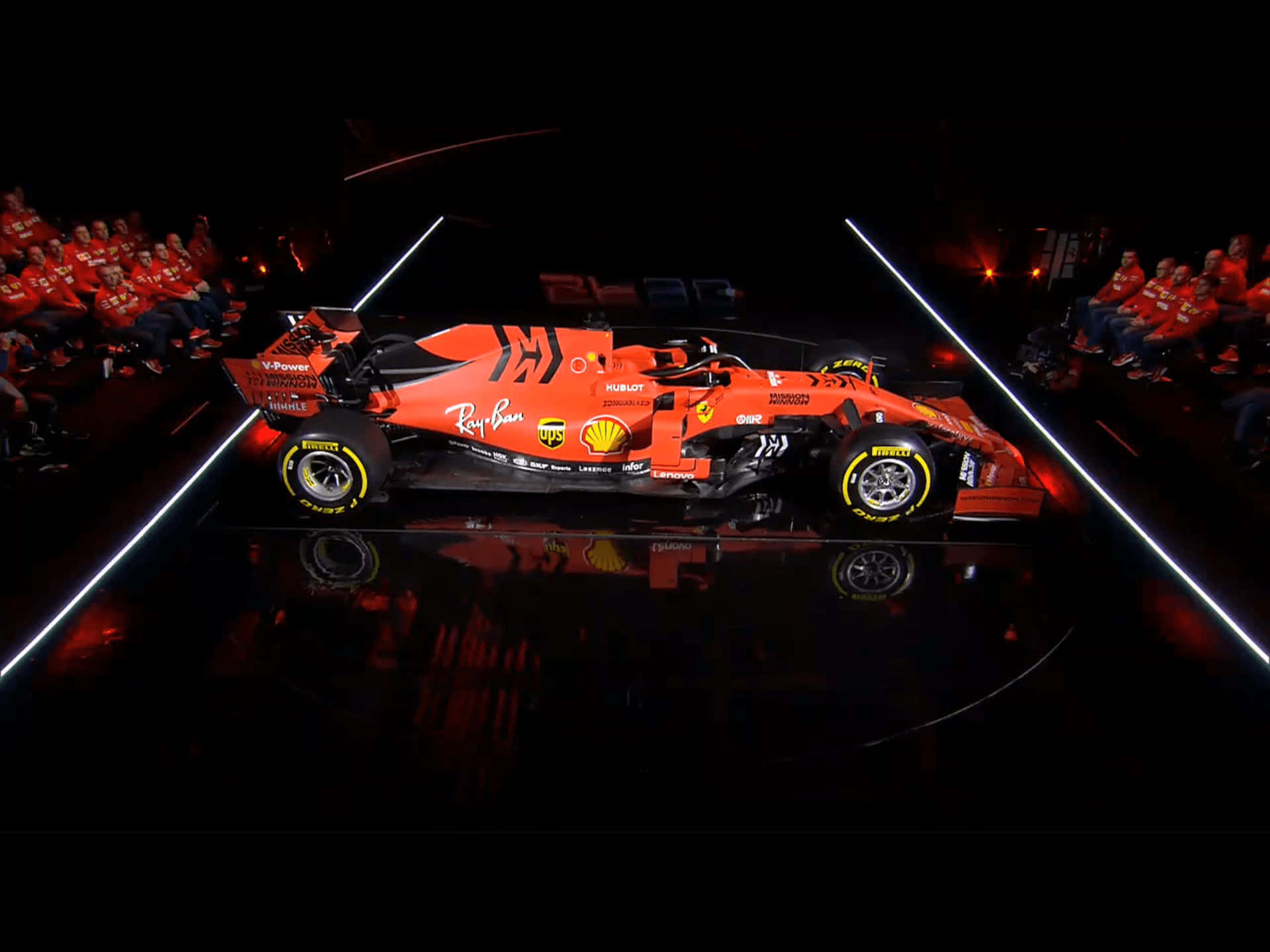速度與力量的化身——法拉利F1 2019 壁紙 — 一架充滿活力的橙色一級方程式賽車在反射舞台上，在明亮的白色燈光下，與身穿紅色的坐席觀眾一同戲劇性地展示。