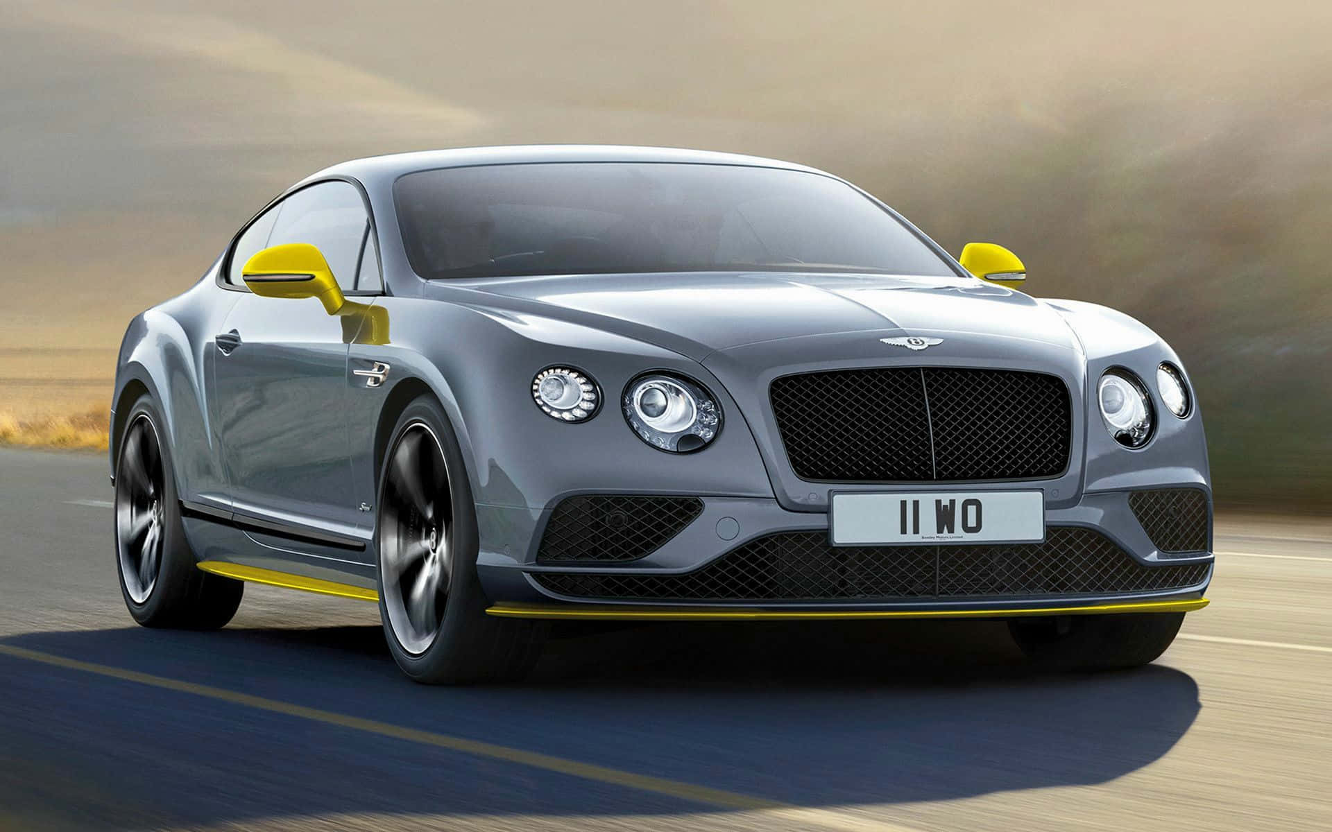 速度與奢華於一車之中 壁紙 — 流線型銀色賓利 Continental GT 帶有醒目黃色點綴，在朦朧金色天空下於沙漠公路上疾馳。