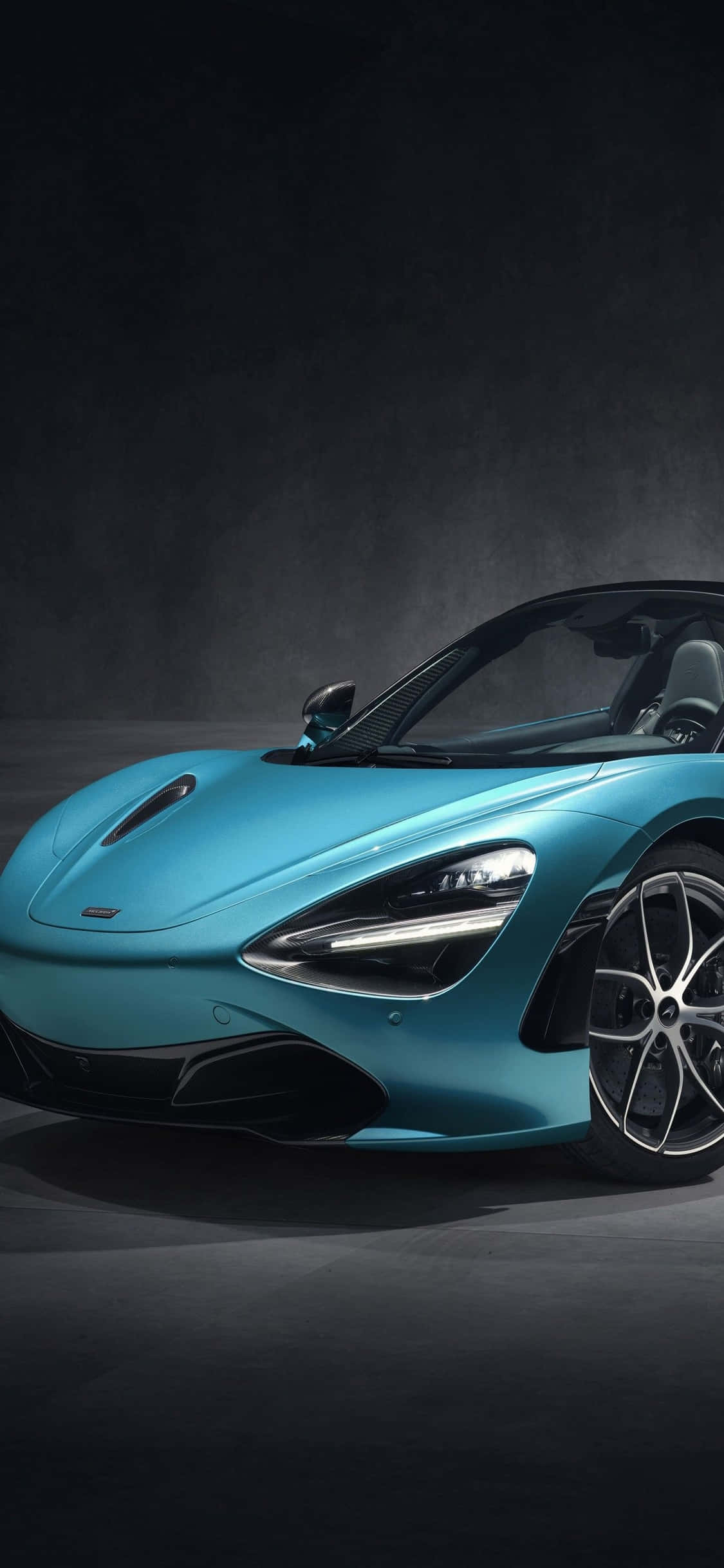 速度與性能的雙重象徵：iPhone Xs 與 McLaren 720S 壁紙 — 一輛時尚的藍綠色McLaren跑車在工作室燈光下，在深色紋理背景上閃耀。