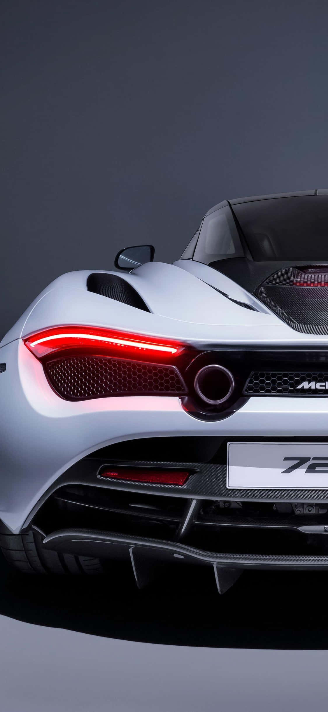 速度與時尚 壁紙 — 一輛時尚的銀色McLaren 720S跑車，帶有發光的紅色尾燈和碳纖維飾邊，背景為深色工作室。