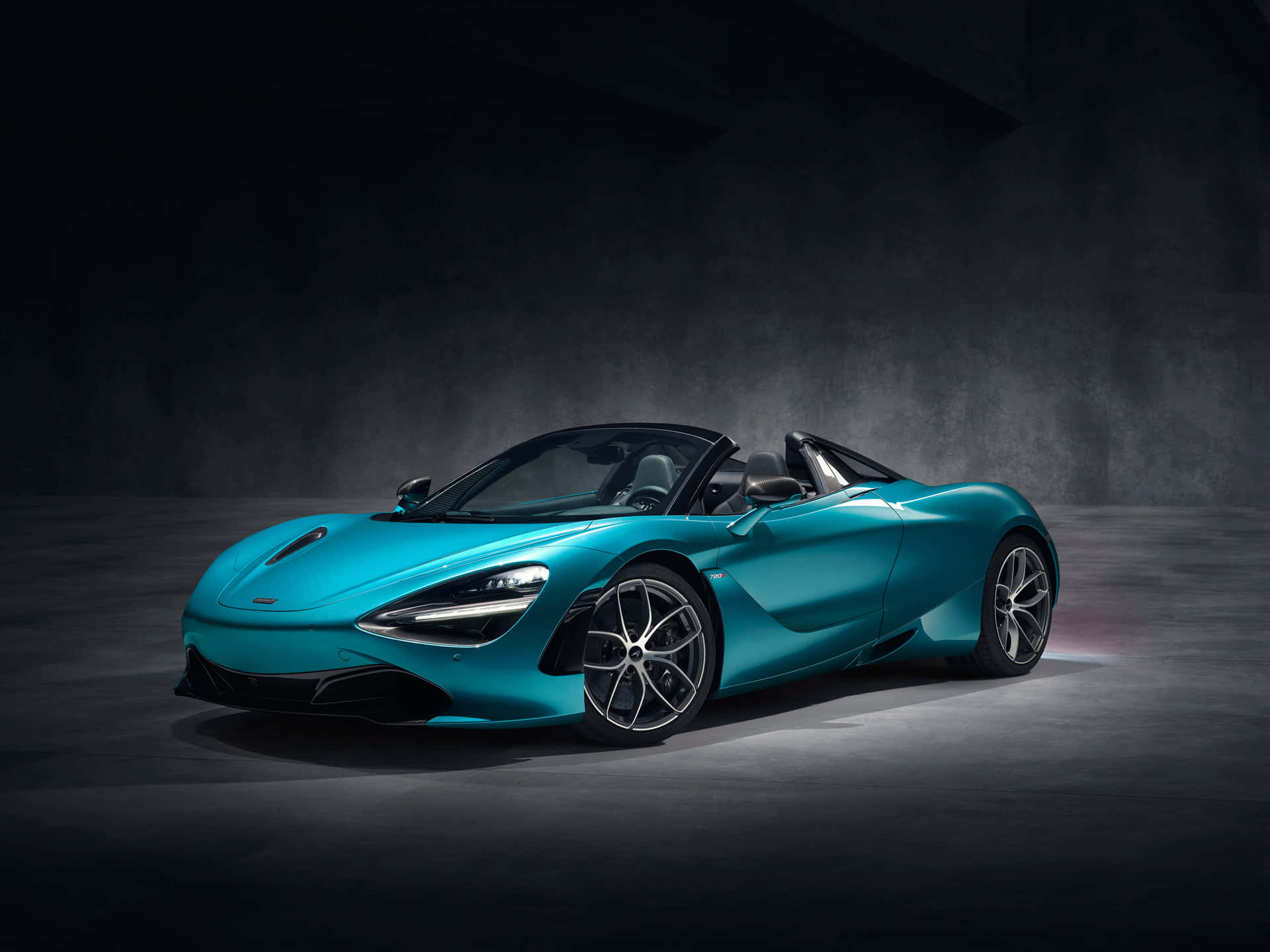 青綠色McLaren 720S Spider敞篷車在黑暗的工作室中，帶有戲劇性的燈光。